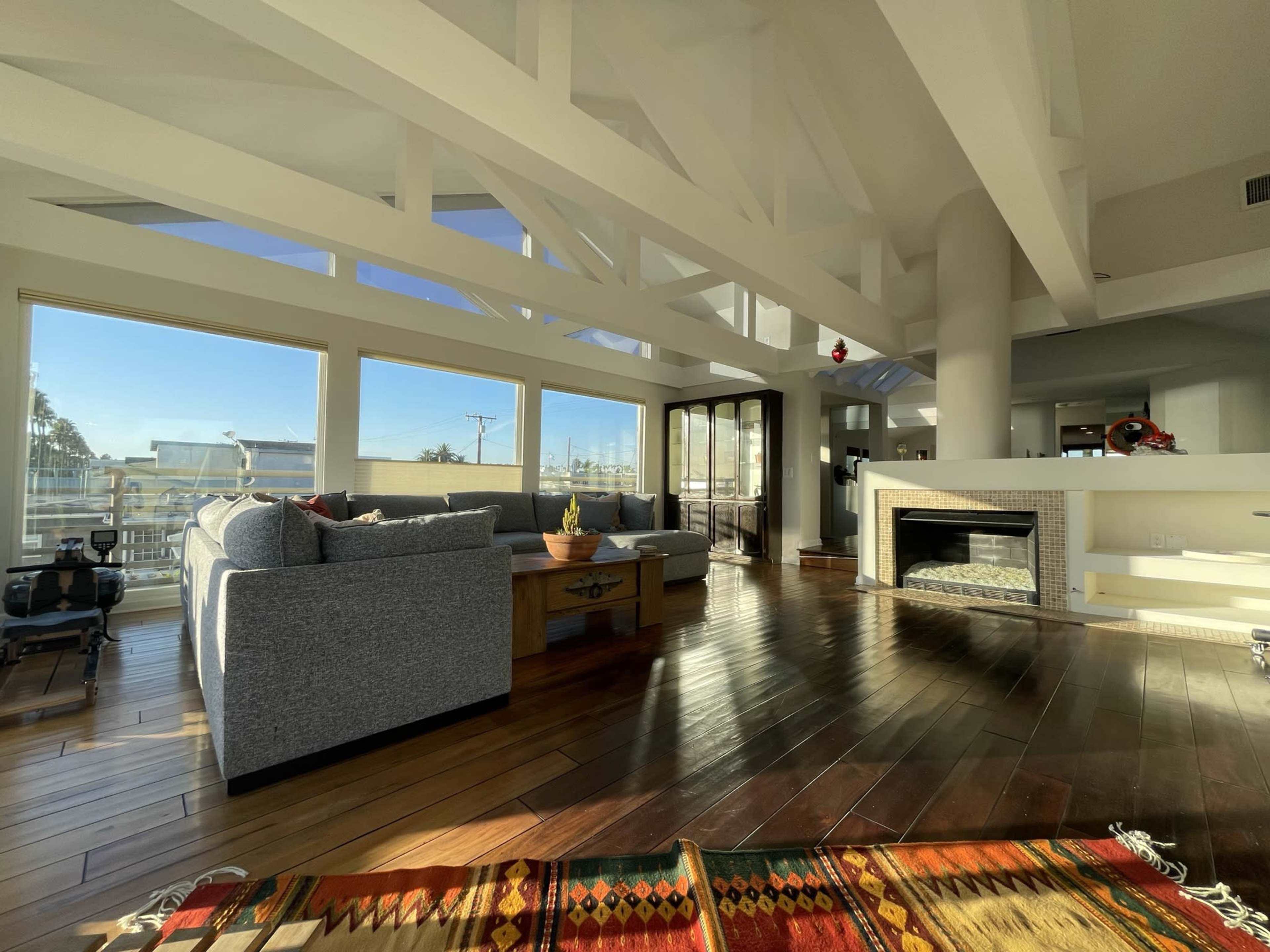 A spacious living room with large windows, wooden floors, and a modern fireplace.