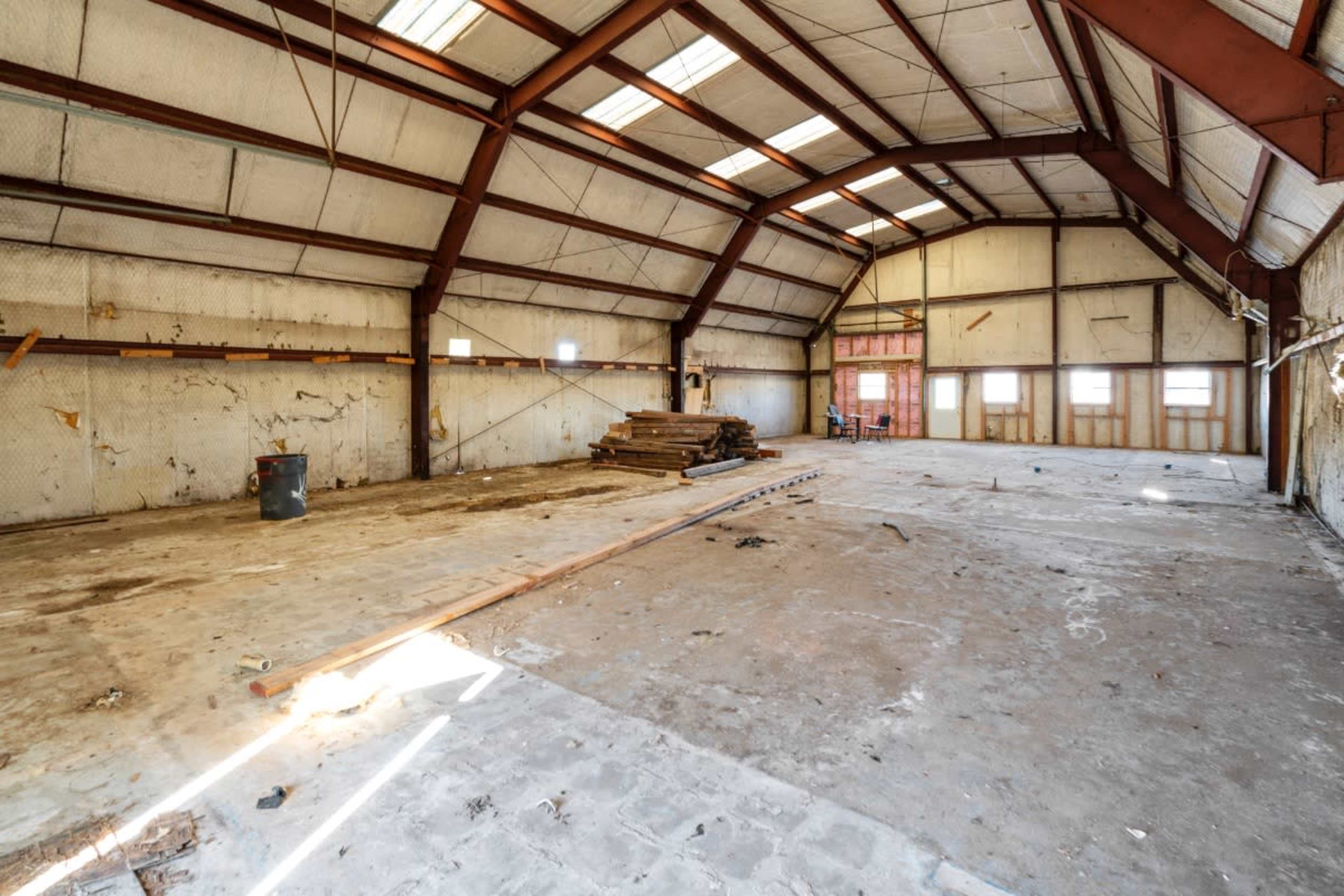 The image shows an empty industrial building with a high ceiling, steel beams, and bare concrete flooring.
