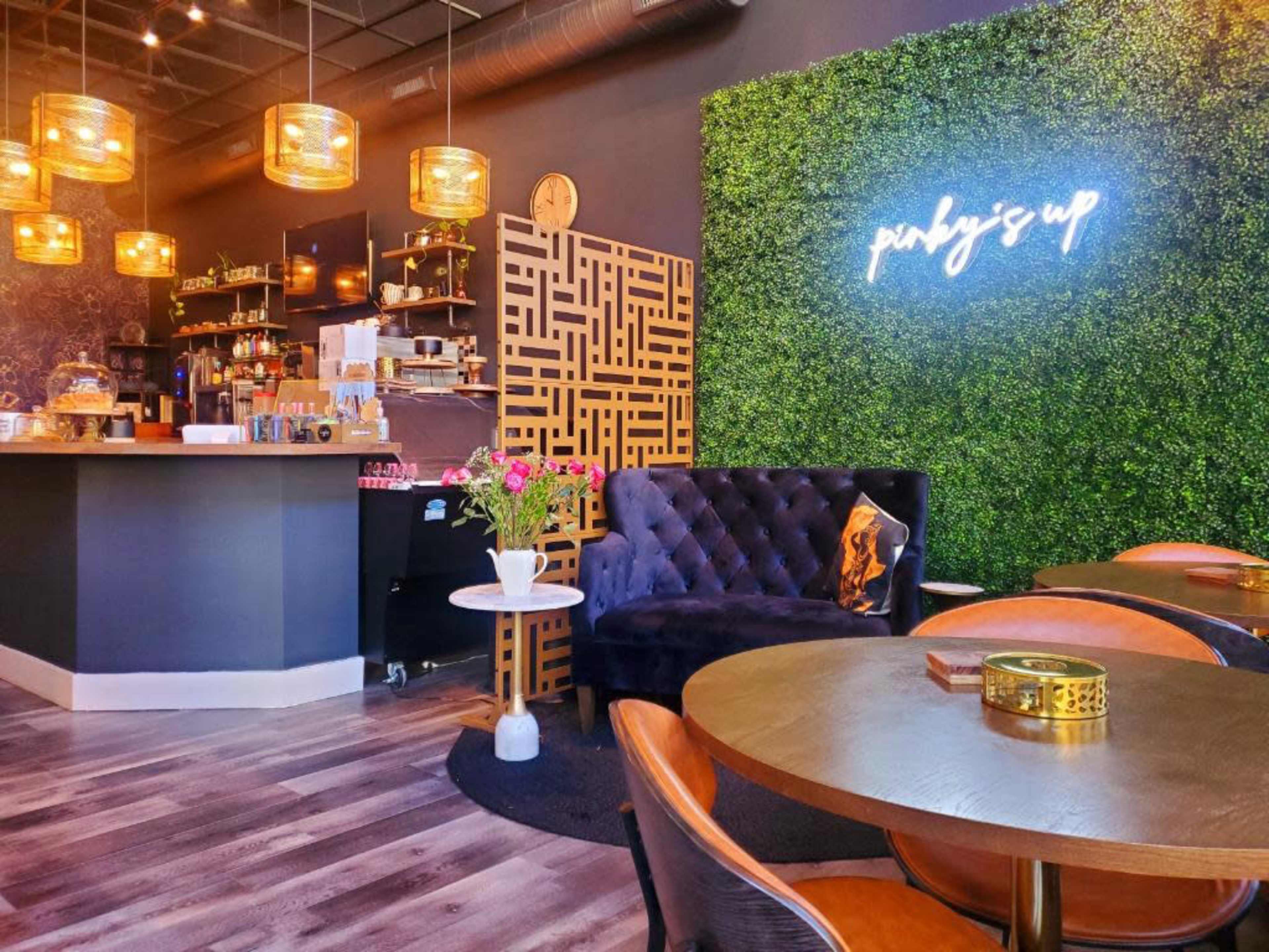 A modern café interior featuring a dark bar area, stylish seating, and a green wall with decorative lighting.