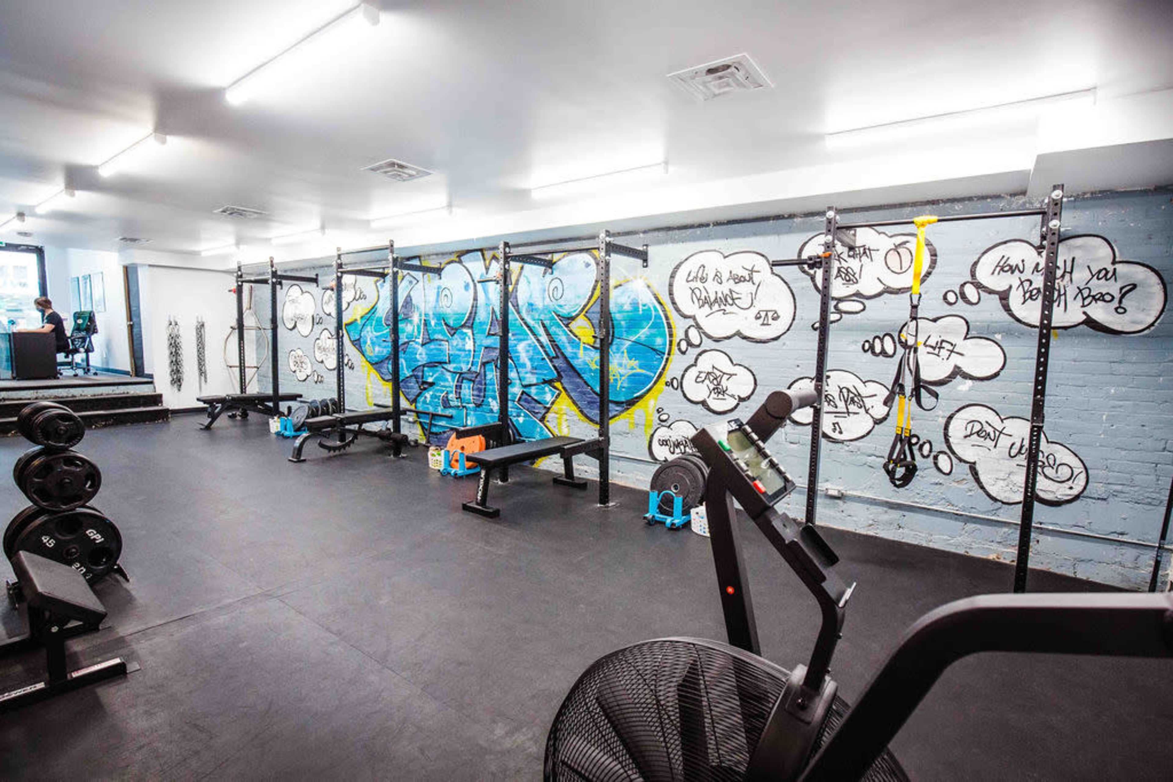 A gym equipped with various weightlifting and exercise equipment, featuring graffiti art on the walls.
