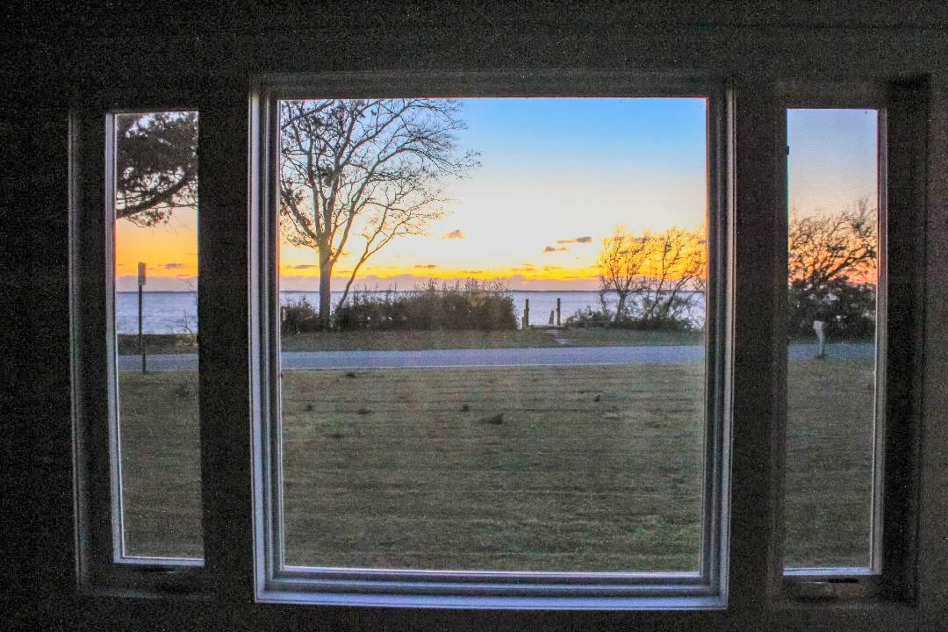 A view of a sunset over a body of water, framed by three large windows in a building.