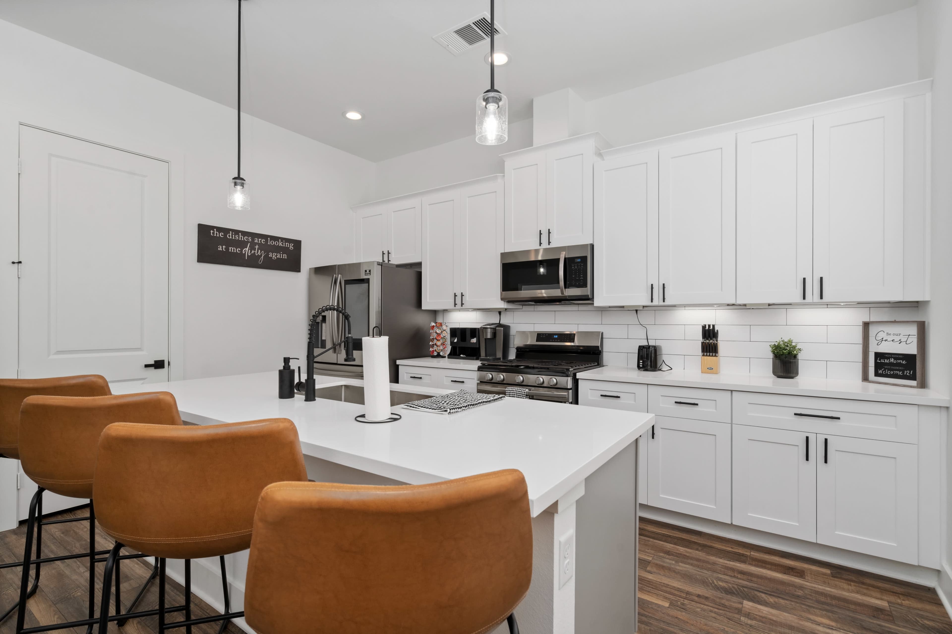 A modern kitchen features white cabinets, stainless steel appliances, and a breakfast bar with brown leather stools.
