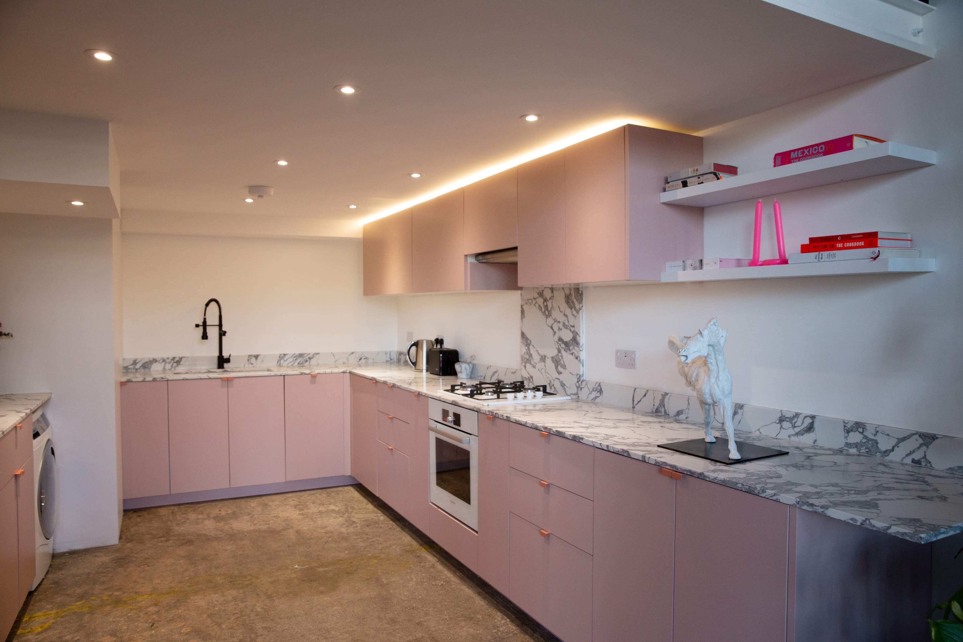 The image shows a modern kitchen with pink cabinetry, a marble countertop, and stainless steel appliances.
