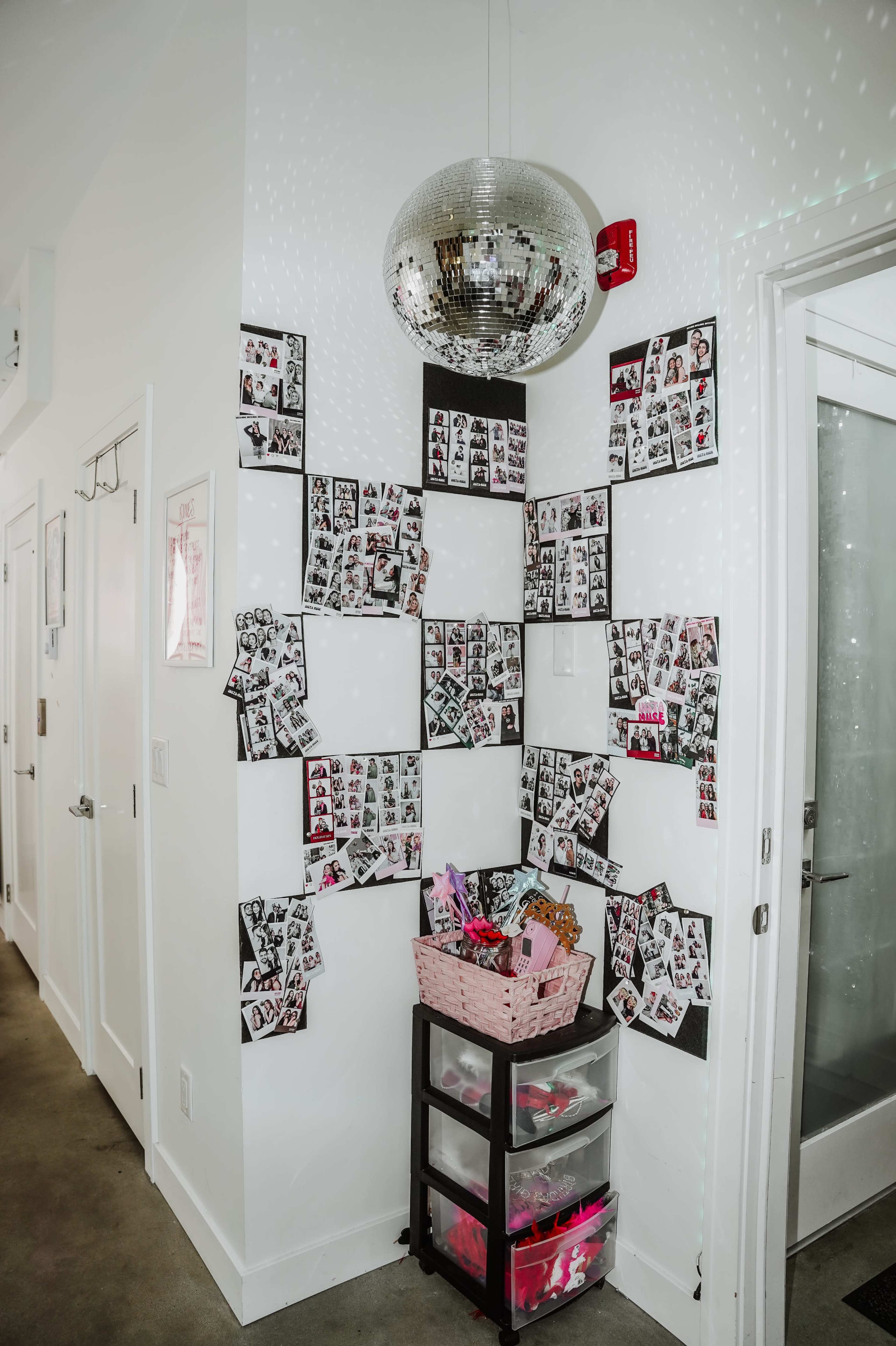 The image shows a corner of a room adorned with black and white photo collages on the wall and a small cart filled with colorful items.