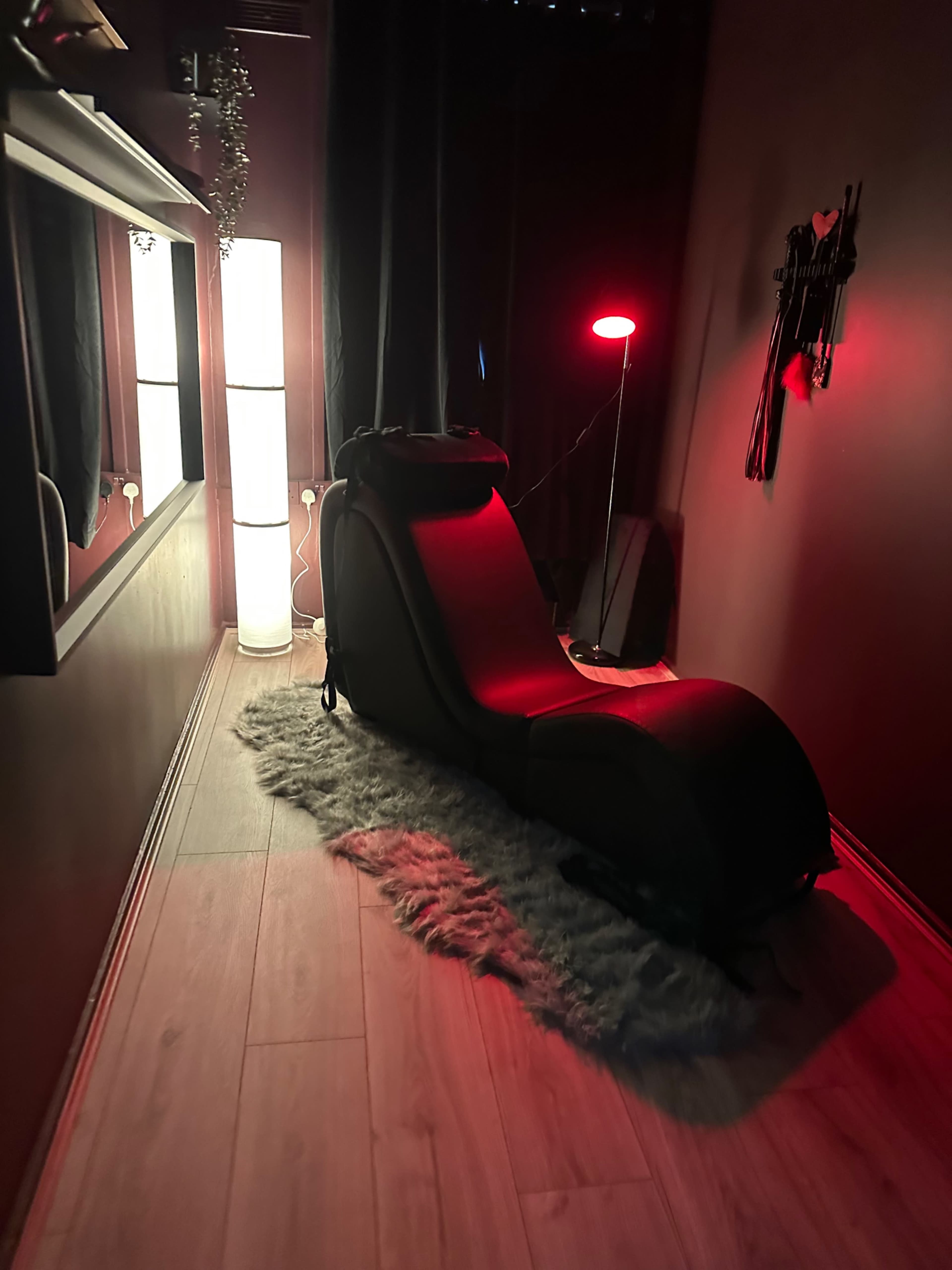 The scene shows a dimly lit room featuring a black lounge chair, a rug, and ambient lighting from lamps.