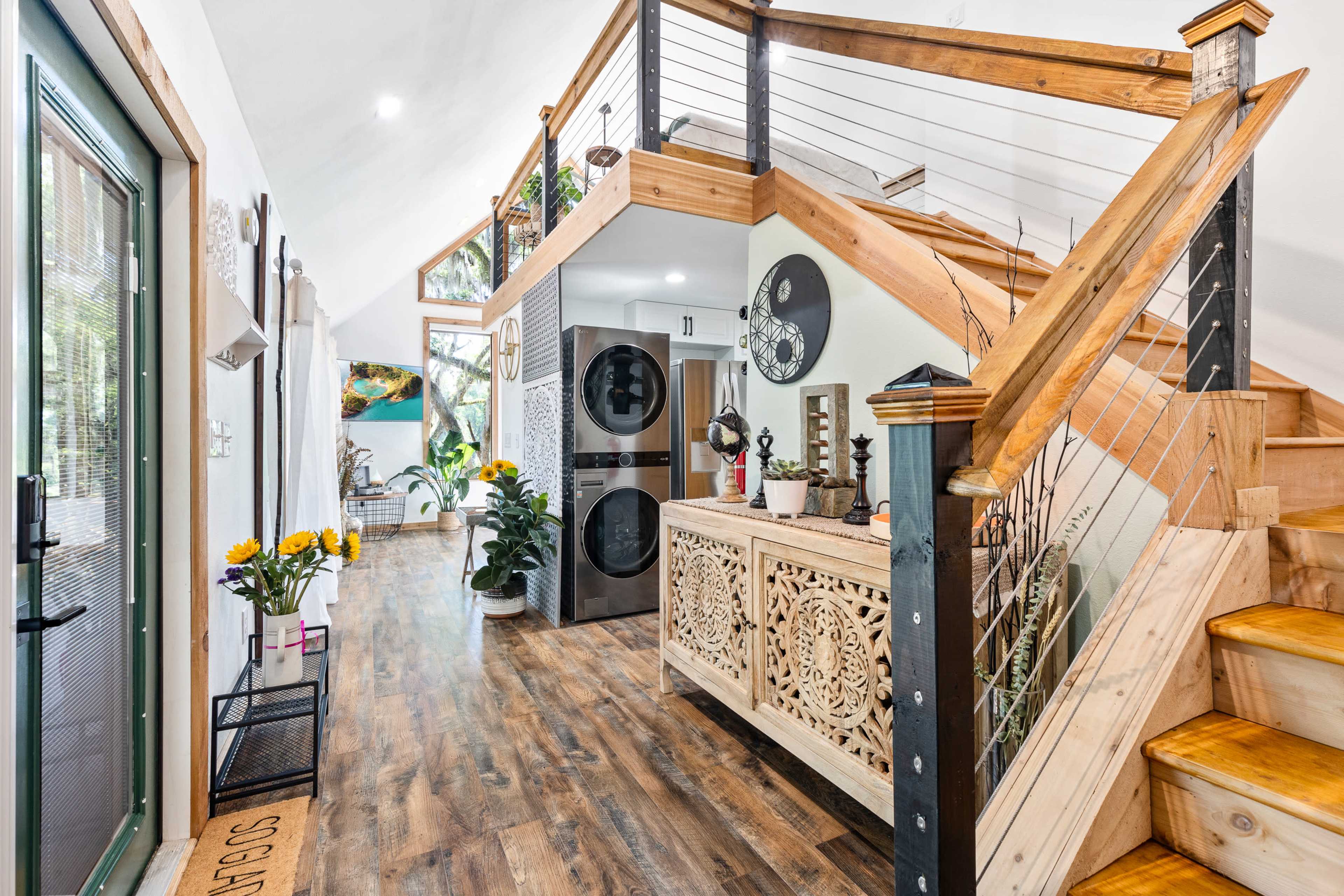 A bright, modern entryway with a wooden staircase, a decorative console table, and large windows that provide natural light.