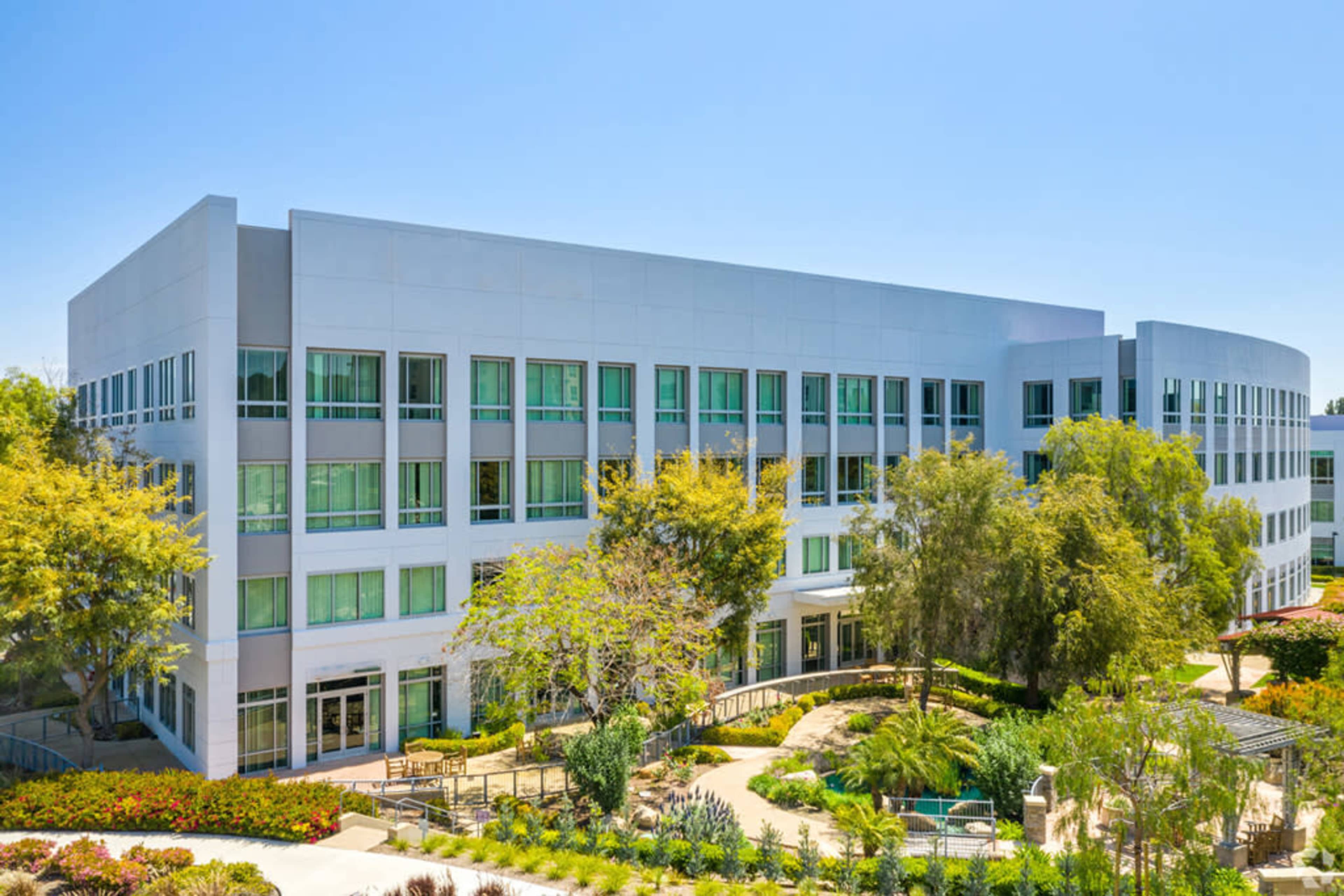 A modern office building features large windows and landscaped greenery surrounding it.
