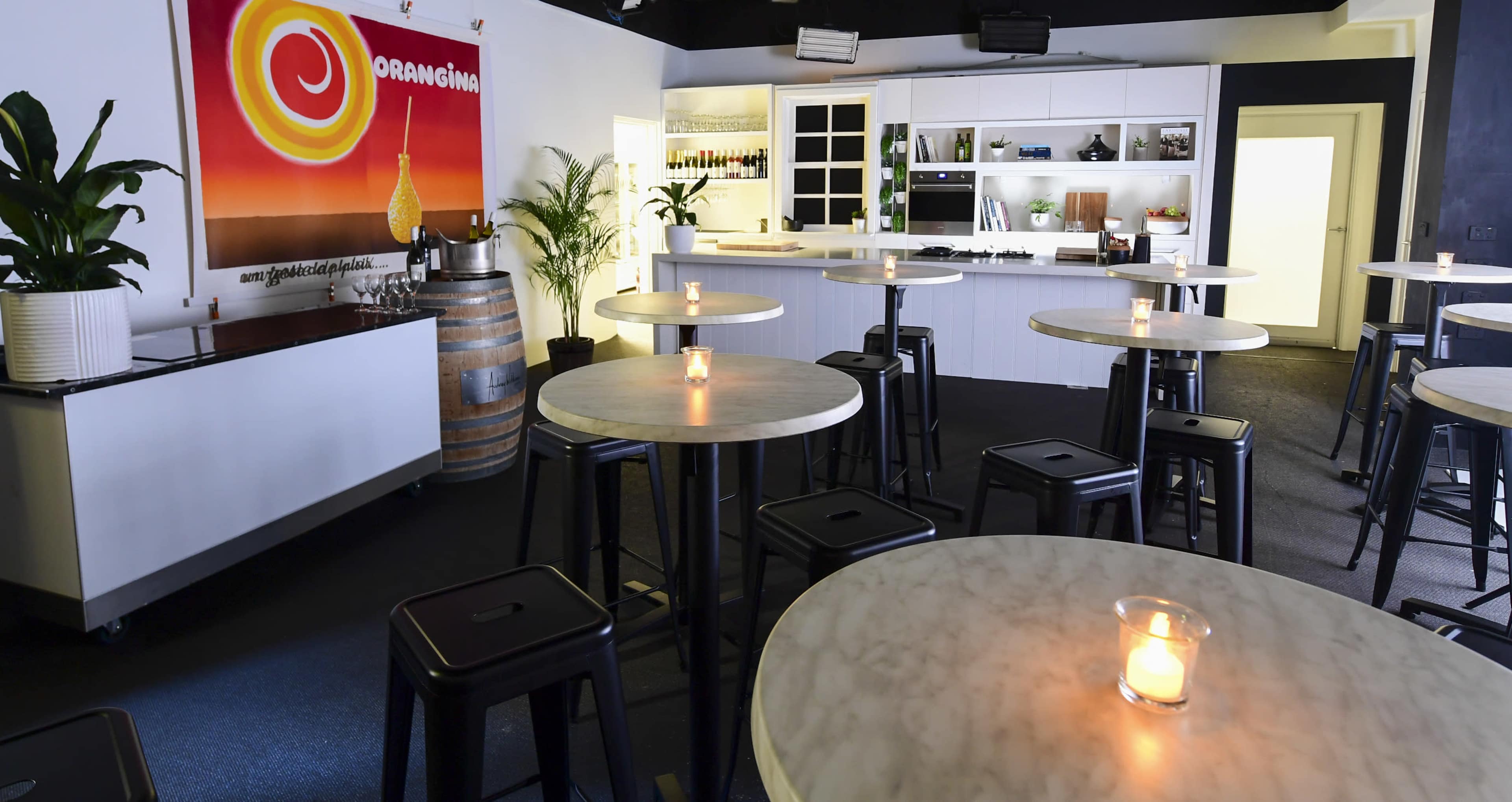 A modern bar area with round marble-top tables, black stools, and a brightly colored mural on the wall, illuminated by candles on the tables.