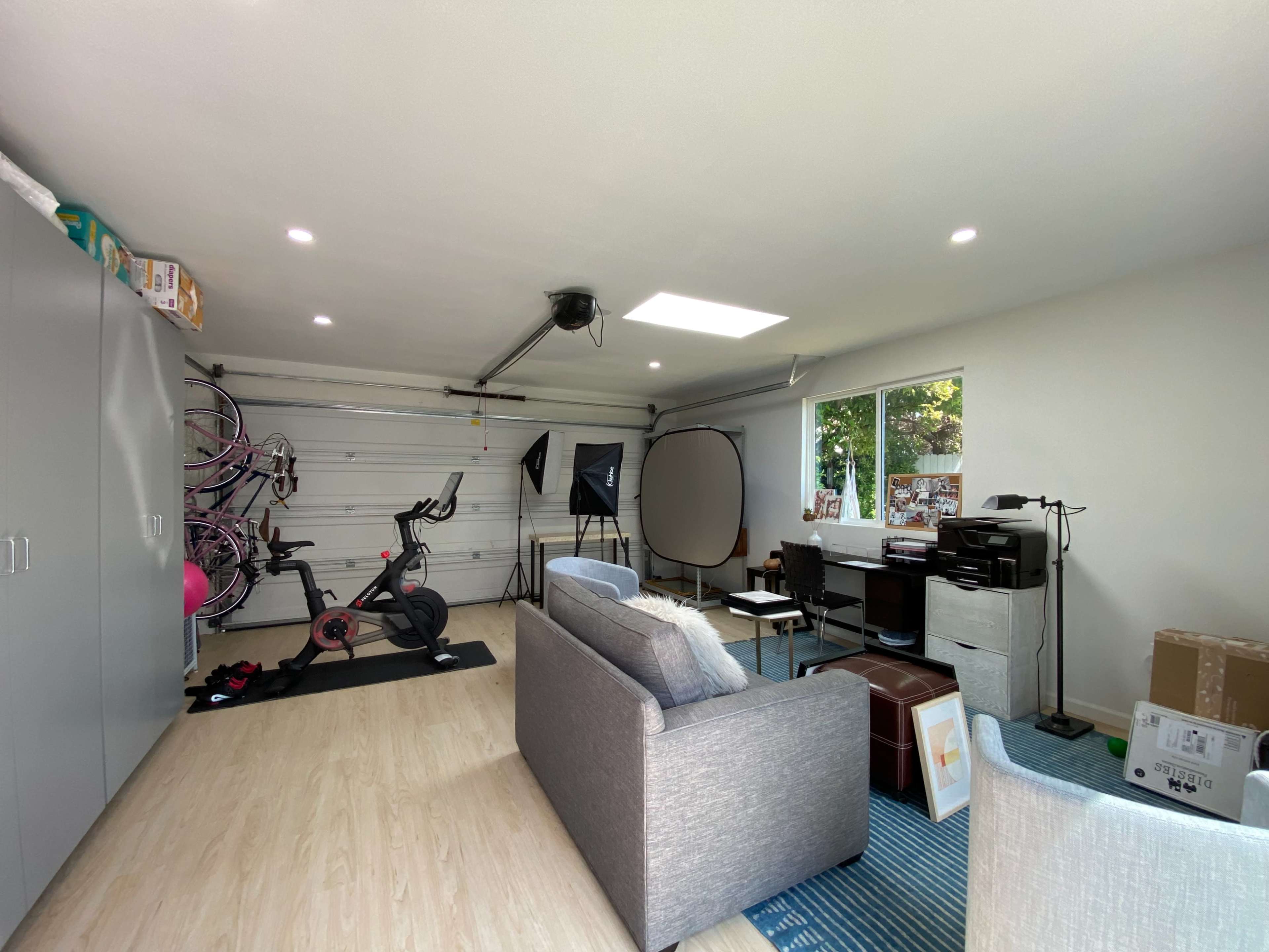 A clean, organized garage converted into a multifunctional space with exercise equipment, a sofa, and office furniture.