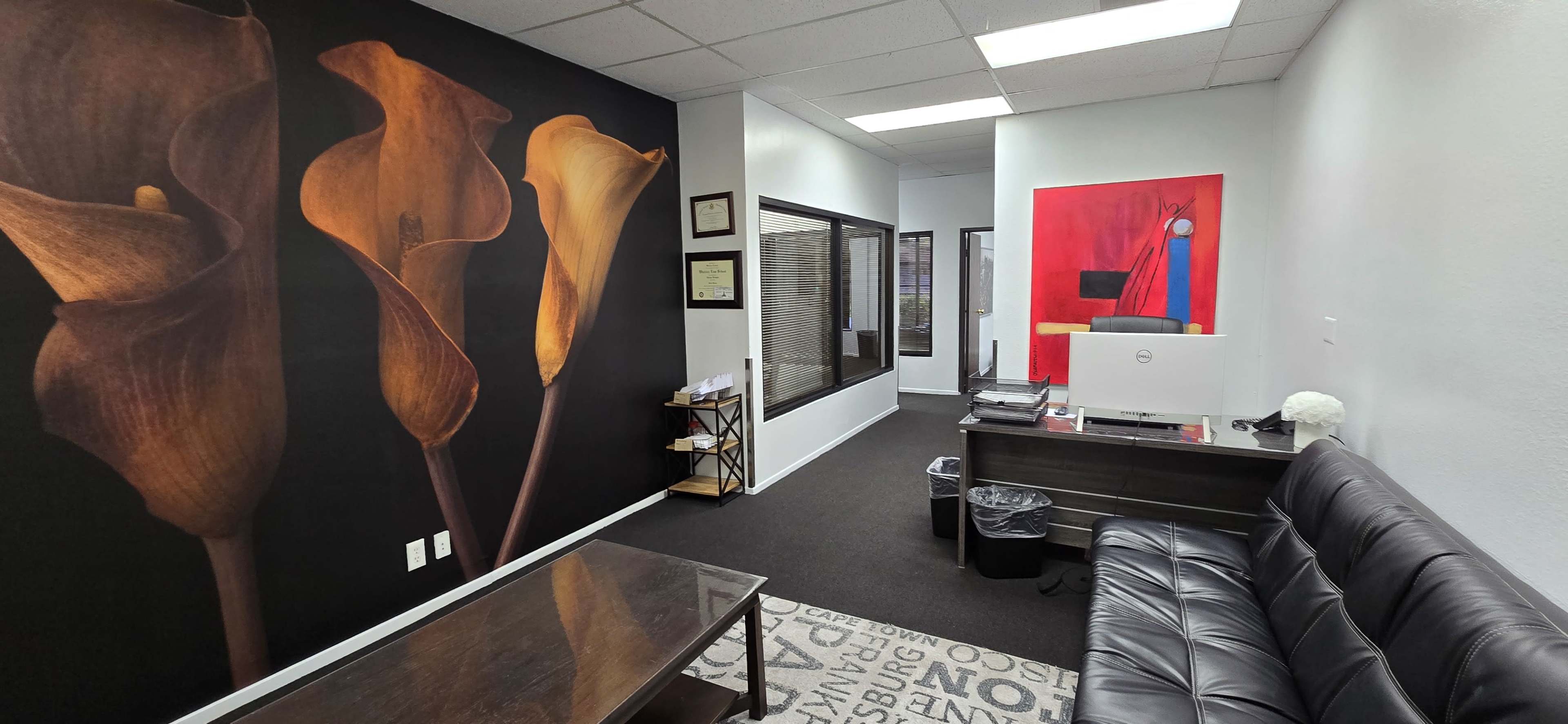 A modern office interior with a black wall featuring floral artwork, a reception area with a desk, and a seating area.