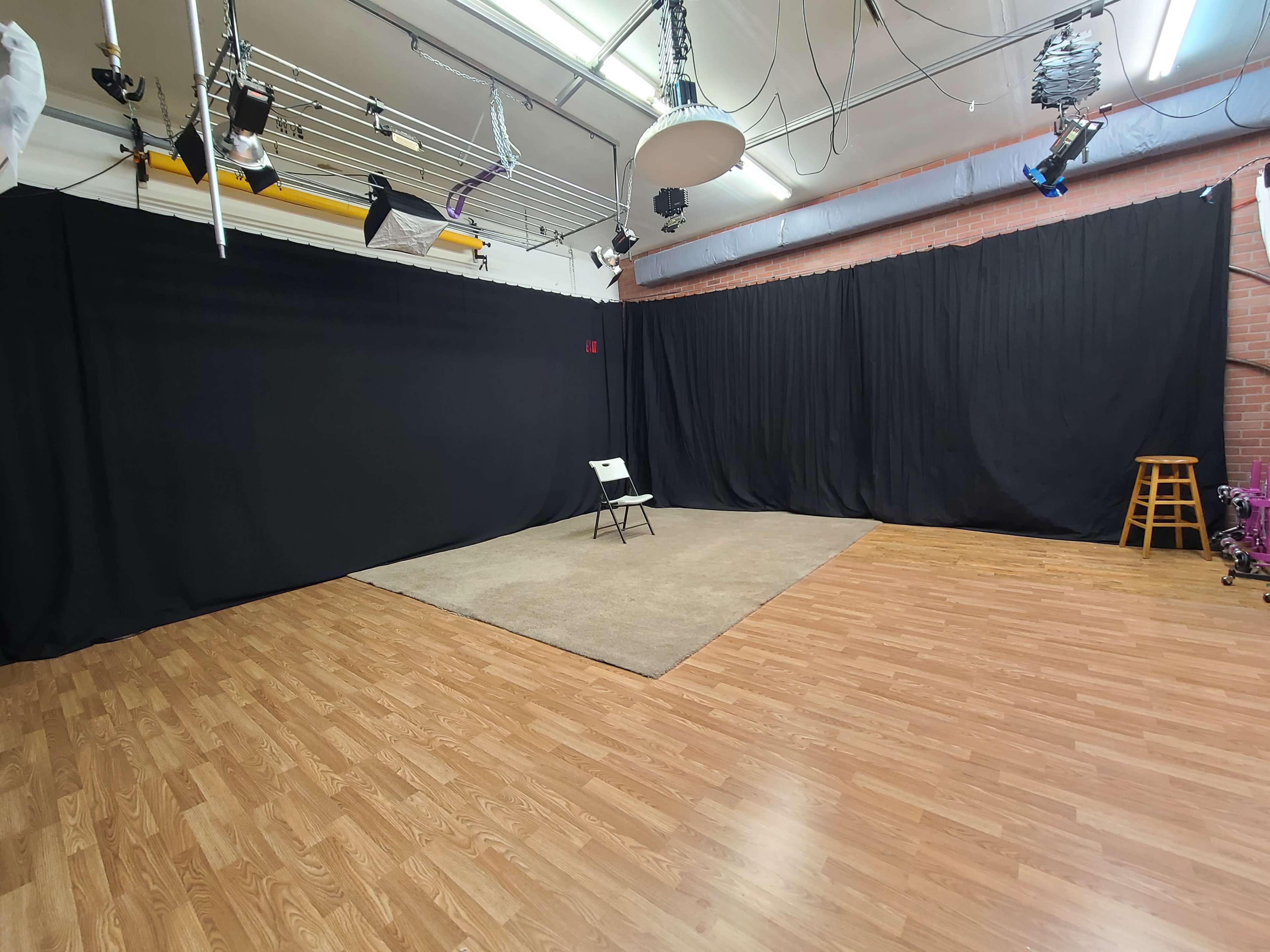 A studio space with black curtains, a beige rug, a single chair in the center, and wooden flooring.
