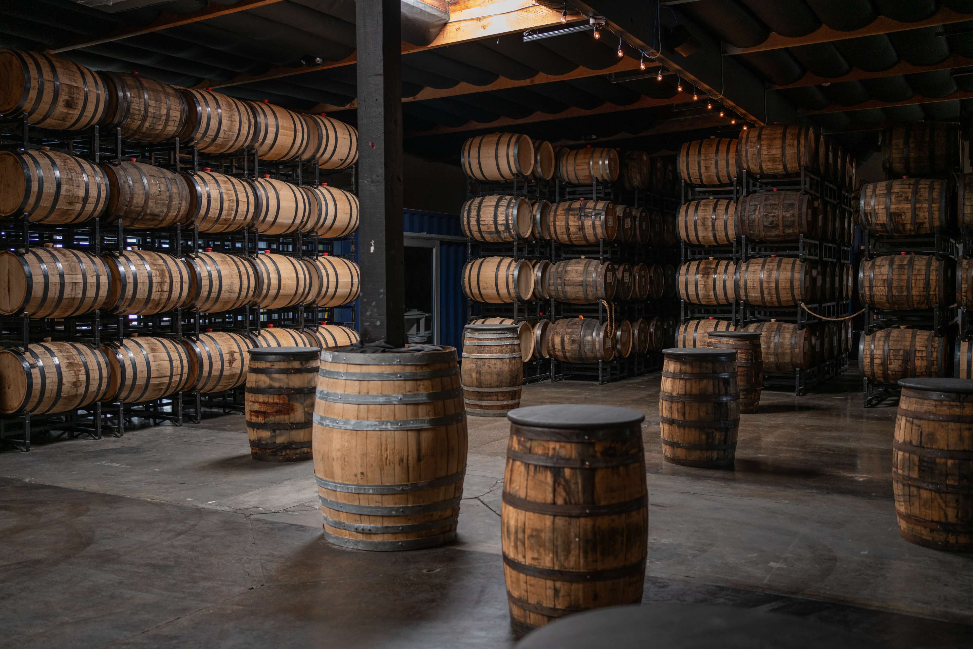 The image shows a storage area filled with numerous wooden barrels stacked on racks, with several smaller barrels arranged on the floor.