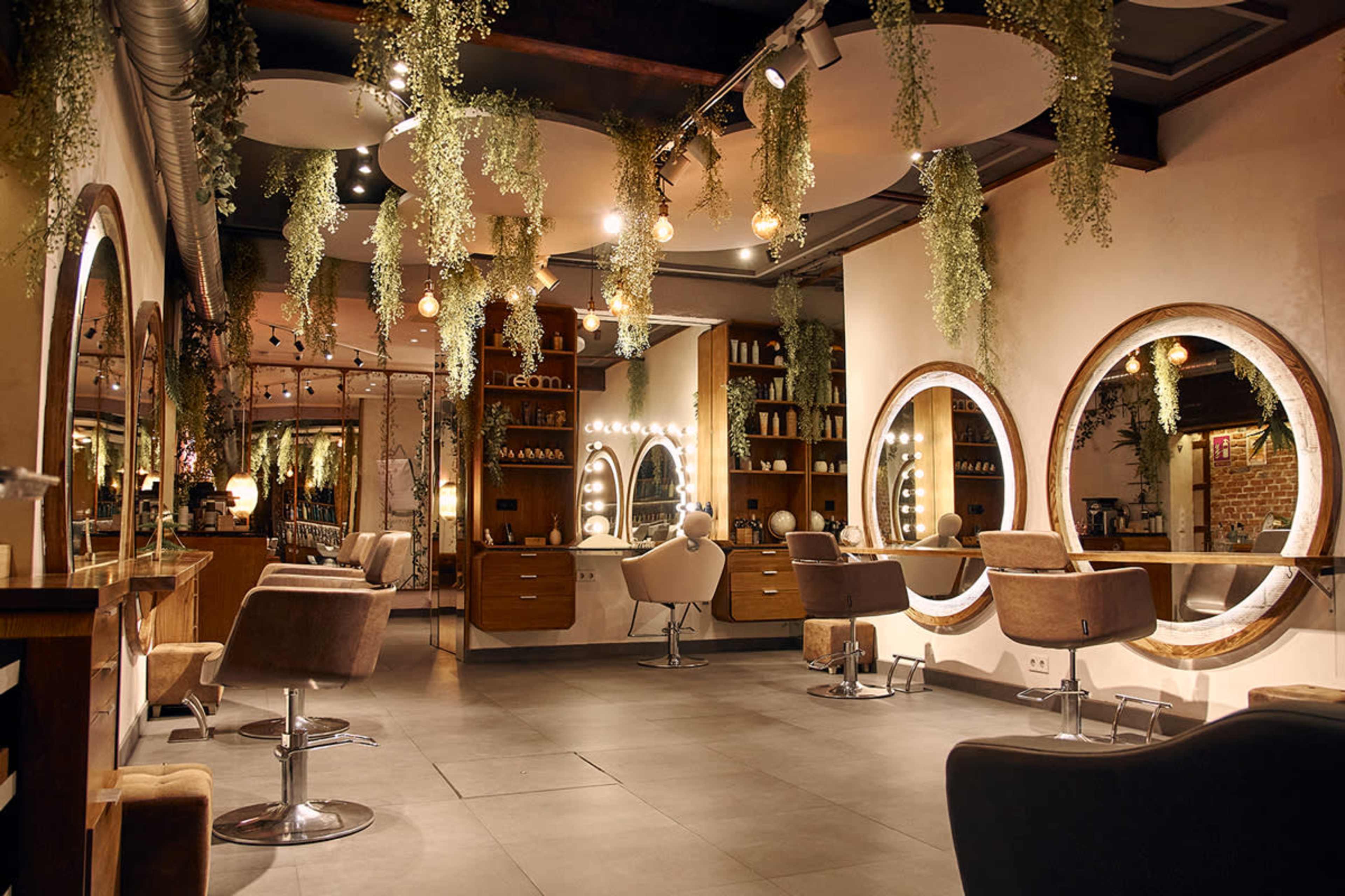 The image shows a modern hair salon featuring multiple circular mirrors, stylish chairs, and hanging greenery.