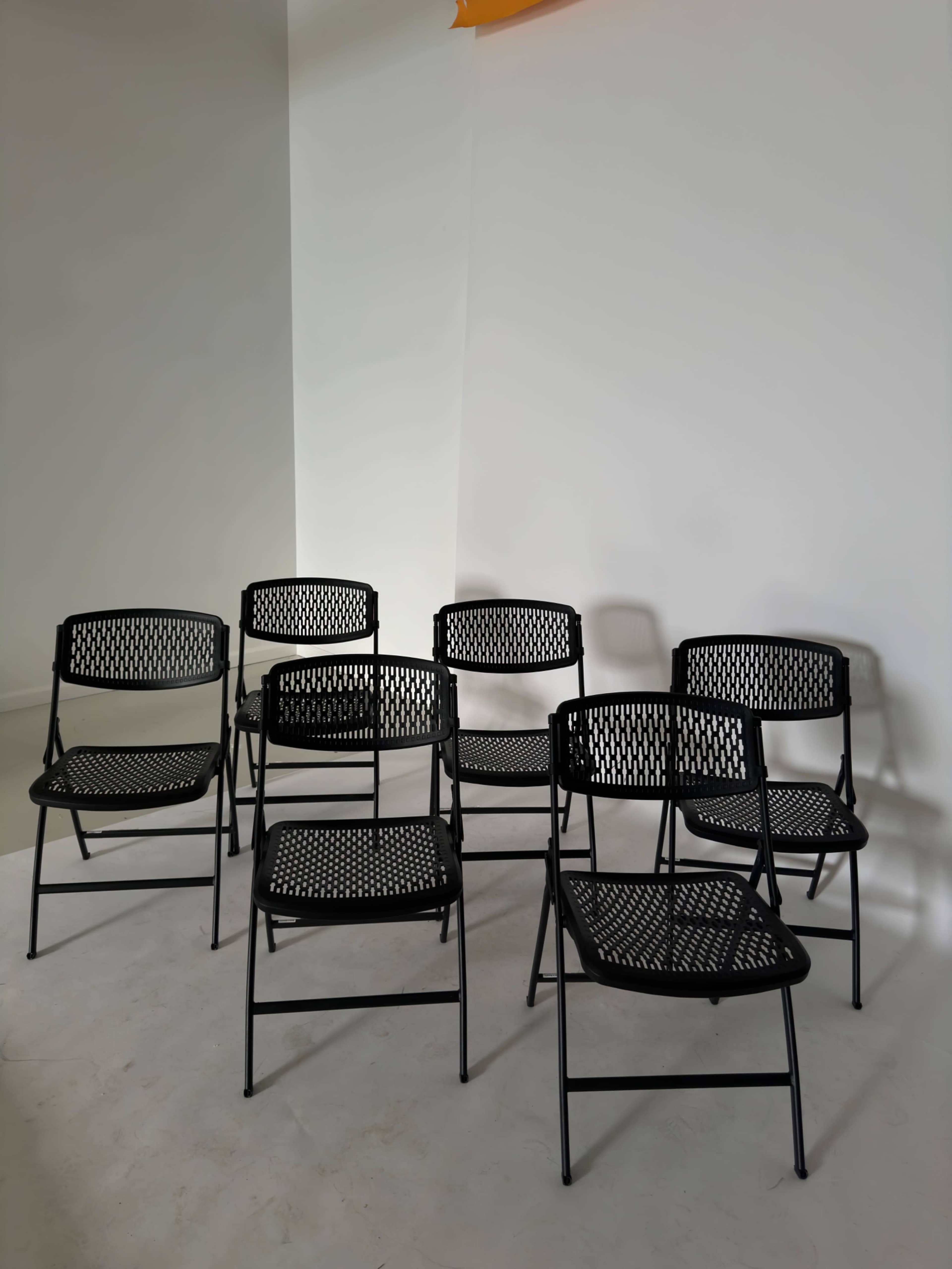 Eight black metal chairs are arranged on a light-colored floor against a plain wall.