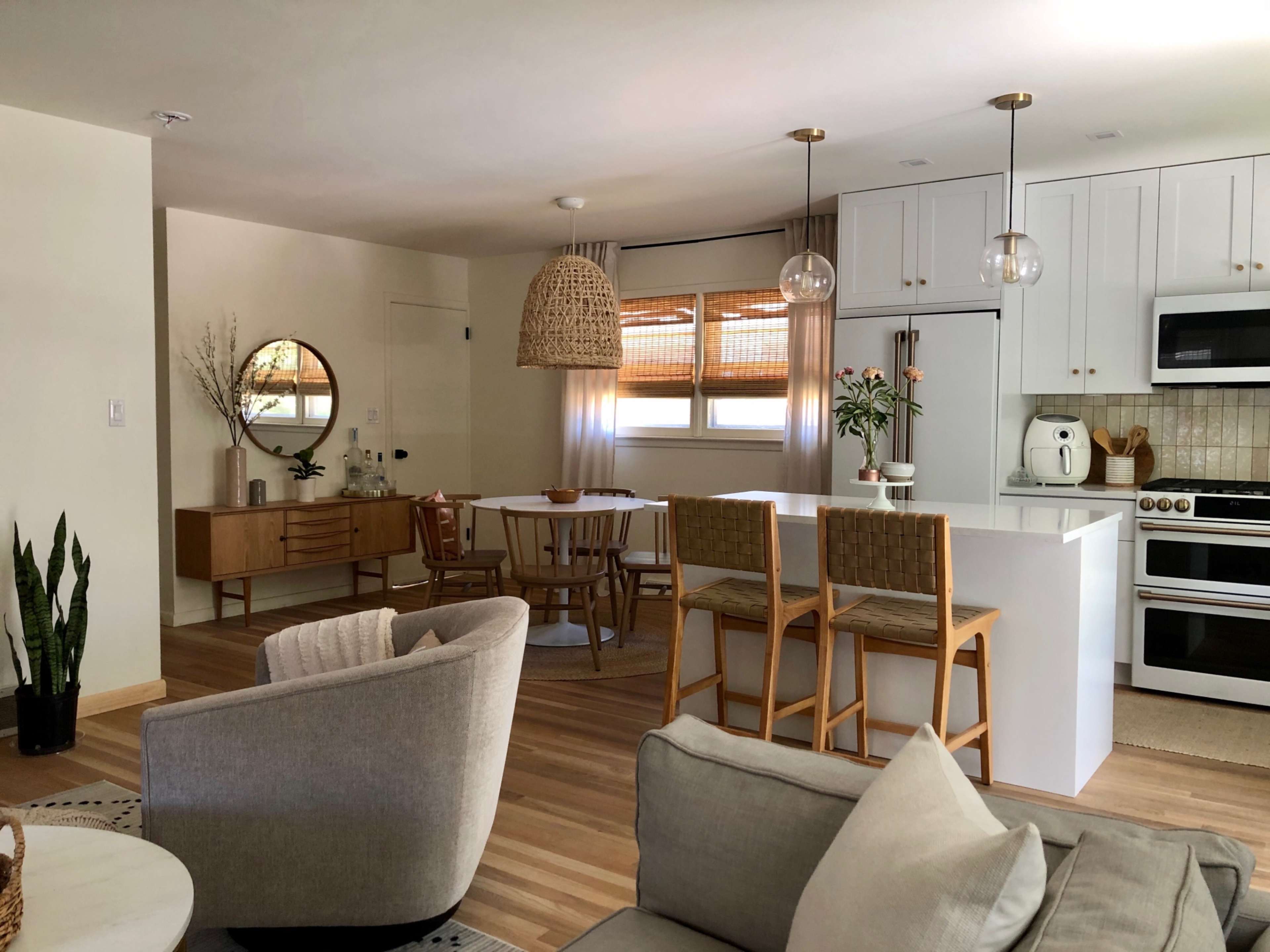 The image shows a modern, open-concept living space with a kitchen island, dining area, and comfortable seating arranged around a coffee table.