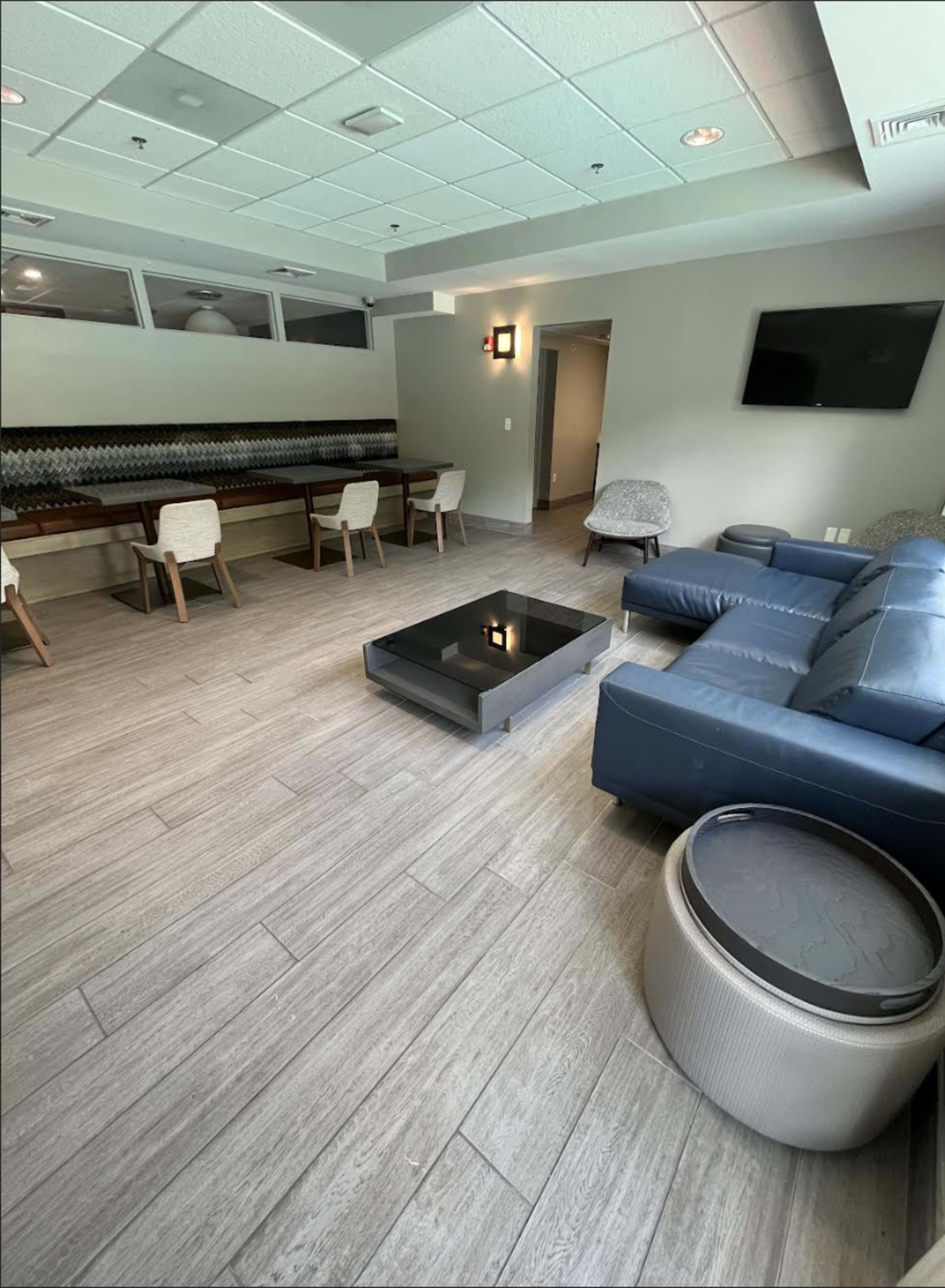 The image shows a modern lounge area with a blue sectional sofa, a coffee table, a bar counter with seating, and a television mounted on the wall.