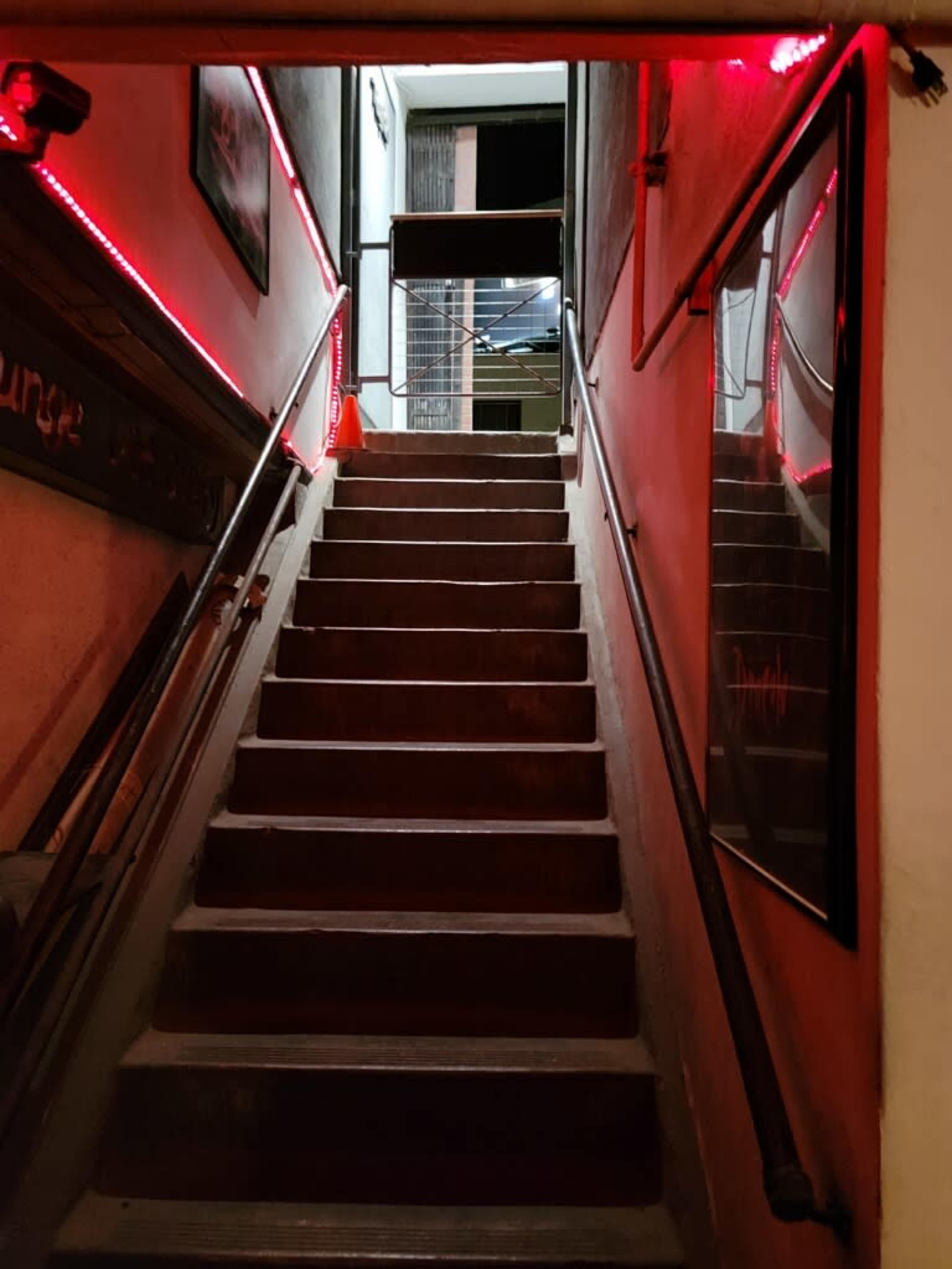 A staircase with red lighting ascends towards an open door at the top.