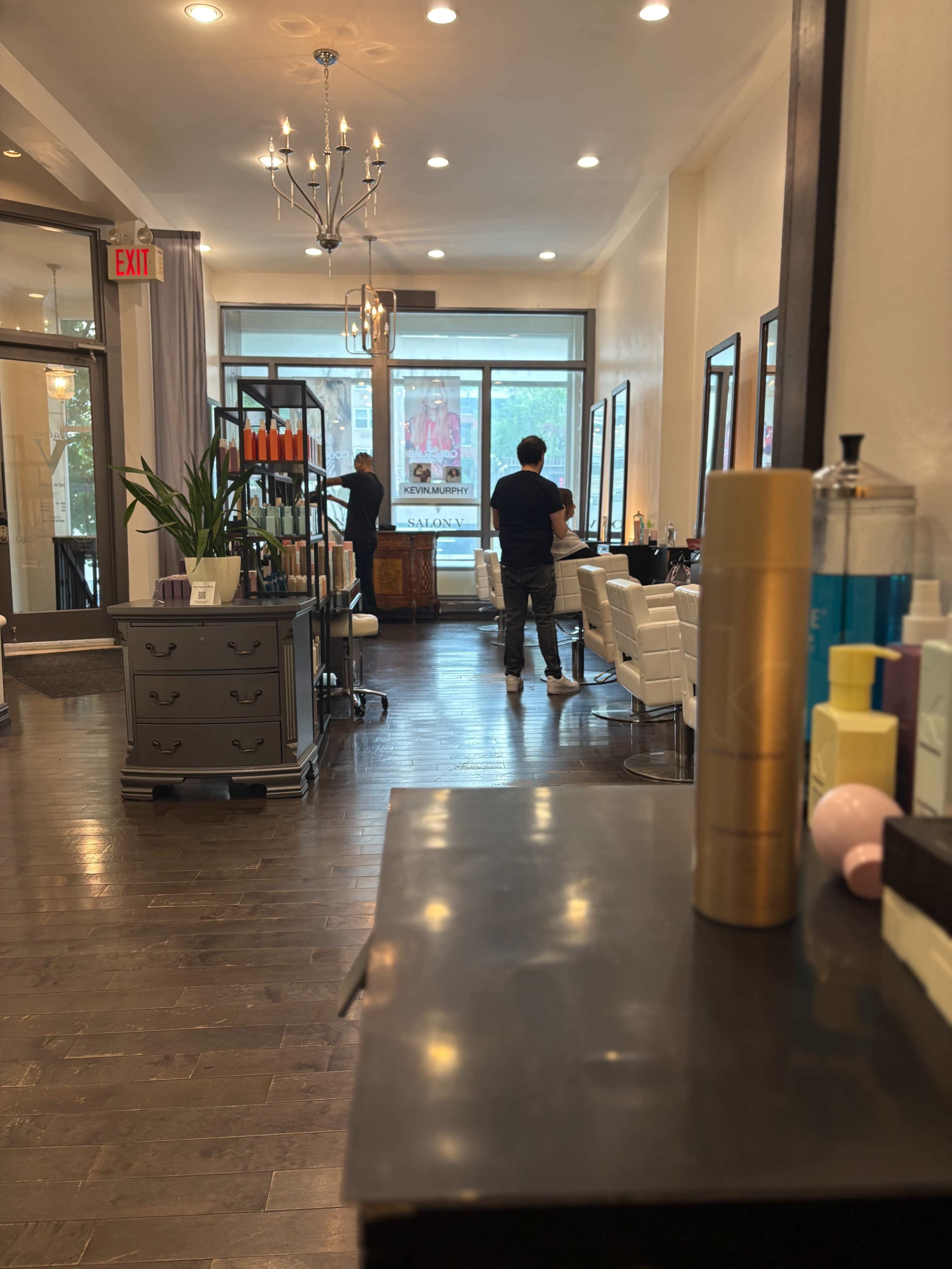 The image shows a stylish salon interior with a reception area, hair styling stations, and products displayed on shelves.