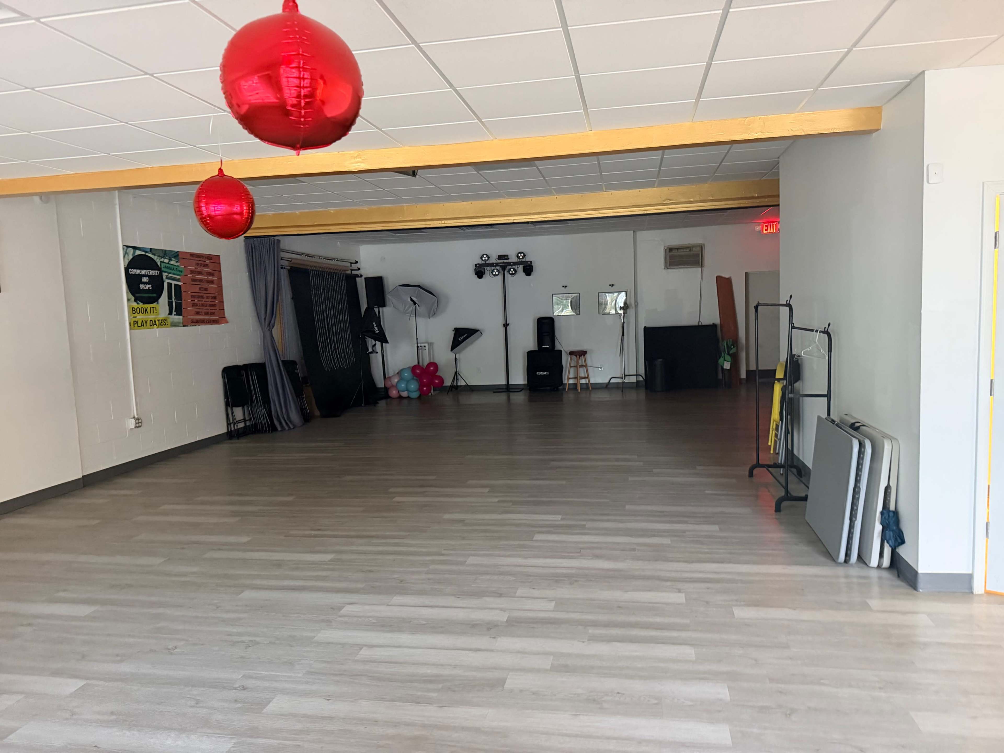 The image shows a spacious, empty room with light-colored flooring, a few decorative red lanterns hanging from the ceiling, and equipment for events positioned along the walls.