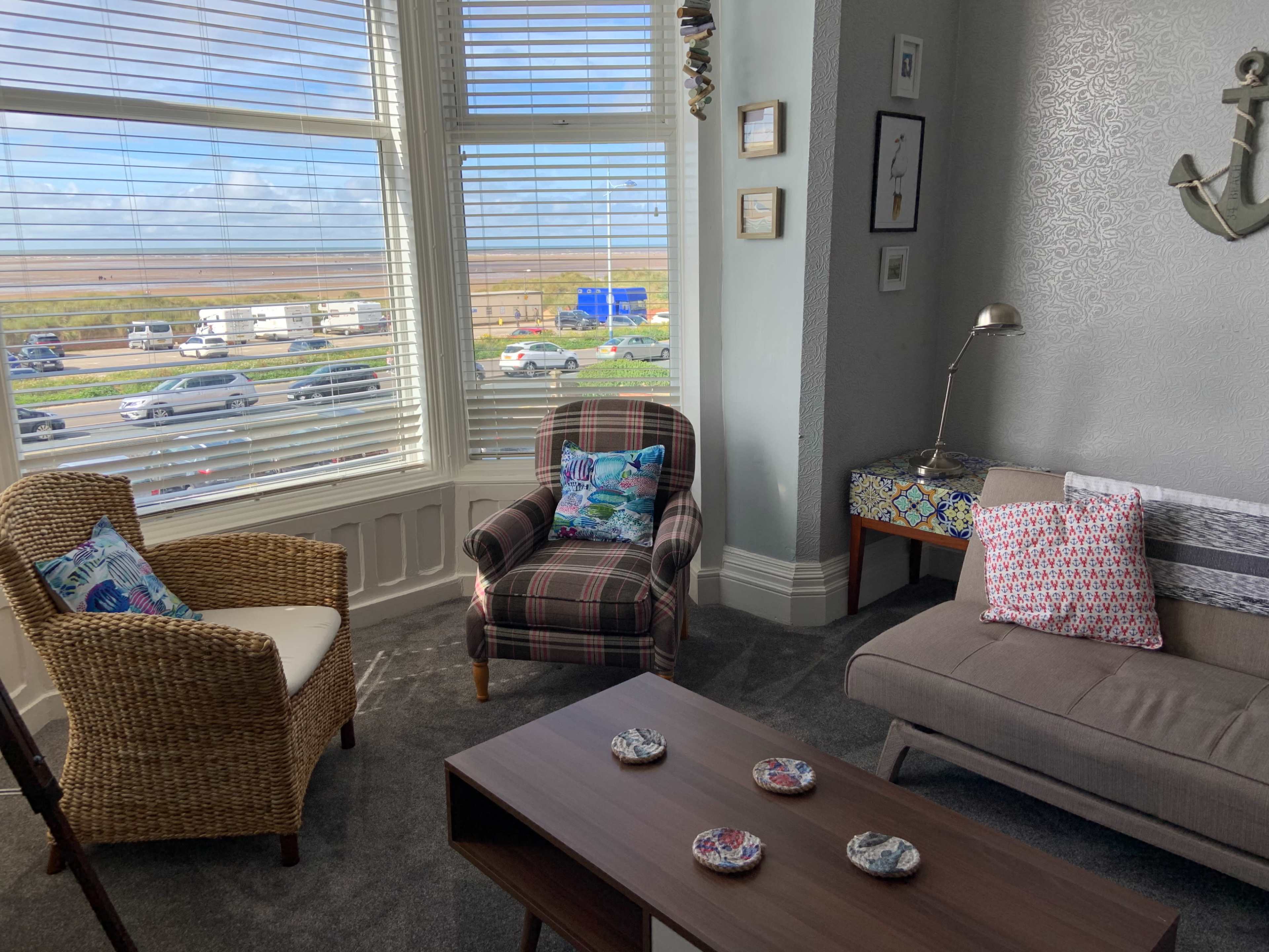 A cozy sitting area features two chairs, a coffee table, and a large window overlooking a busy road and scenic landscape.