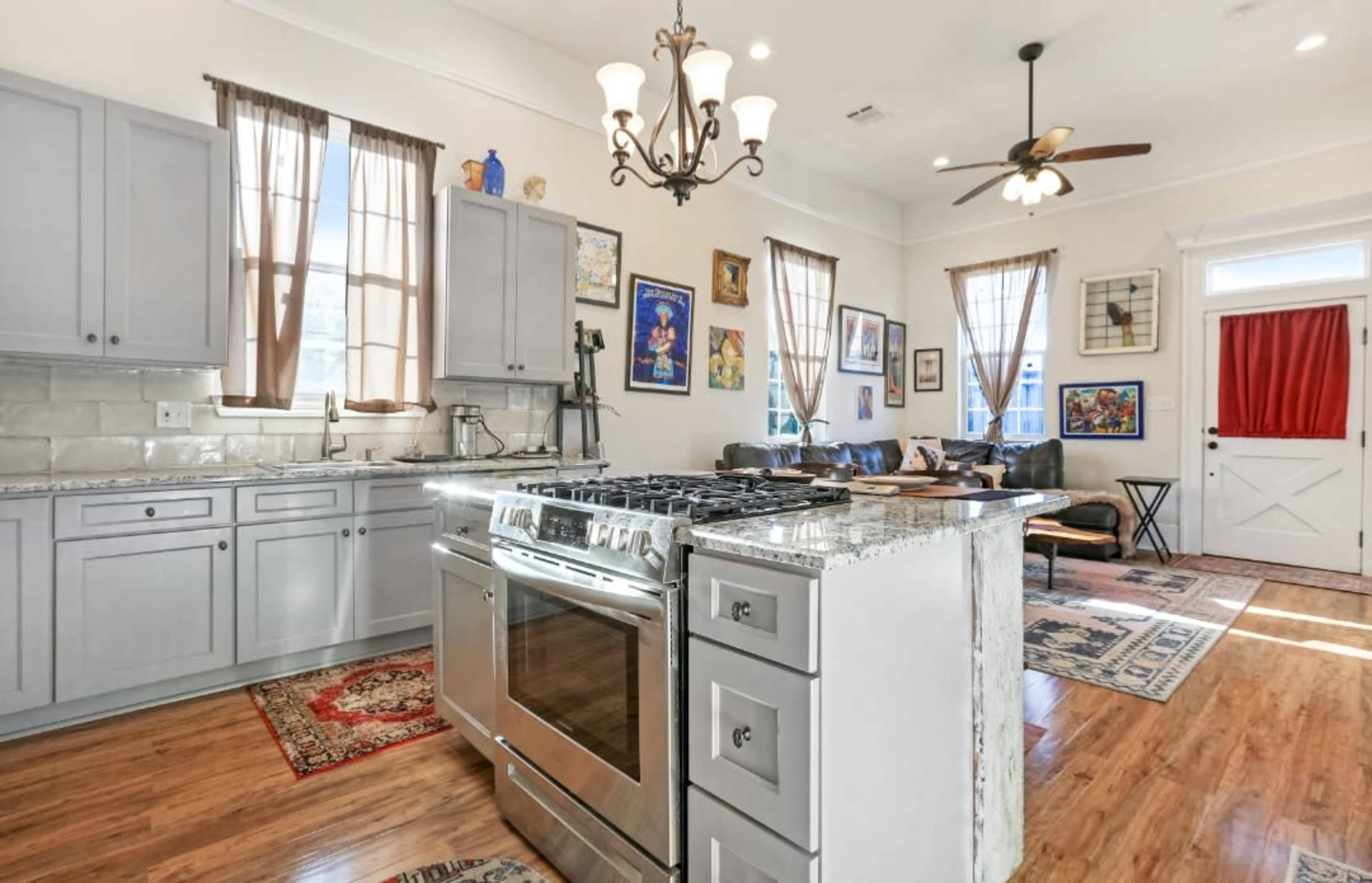 A spacious kitchen features gray cabinets, a large stainless steel stove, and a stone countertop, with a living area visible in the background.
