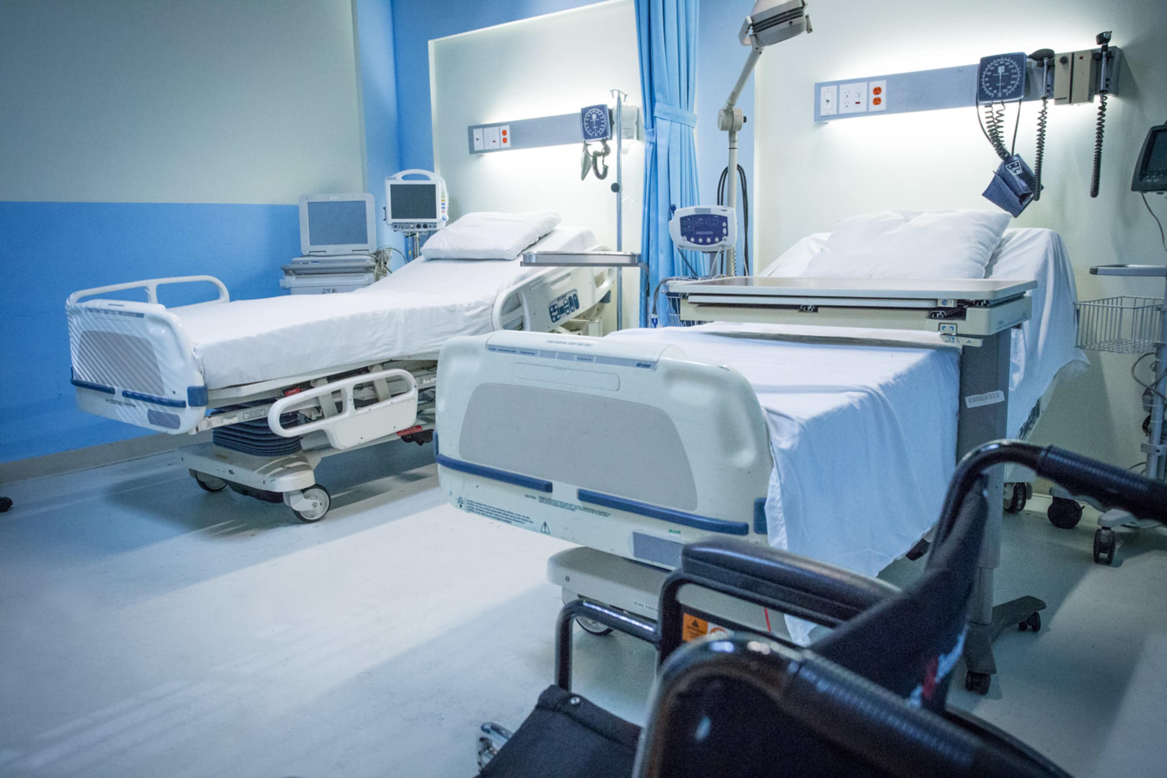 A hospital room featuring two empty hospital beds with medical equipment nearby.