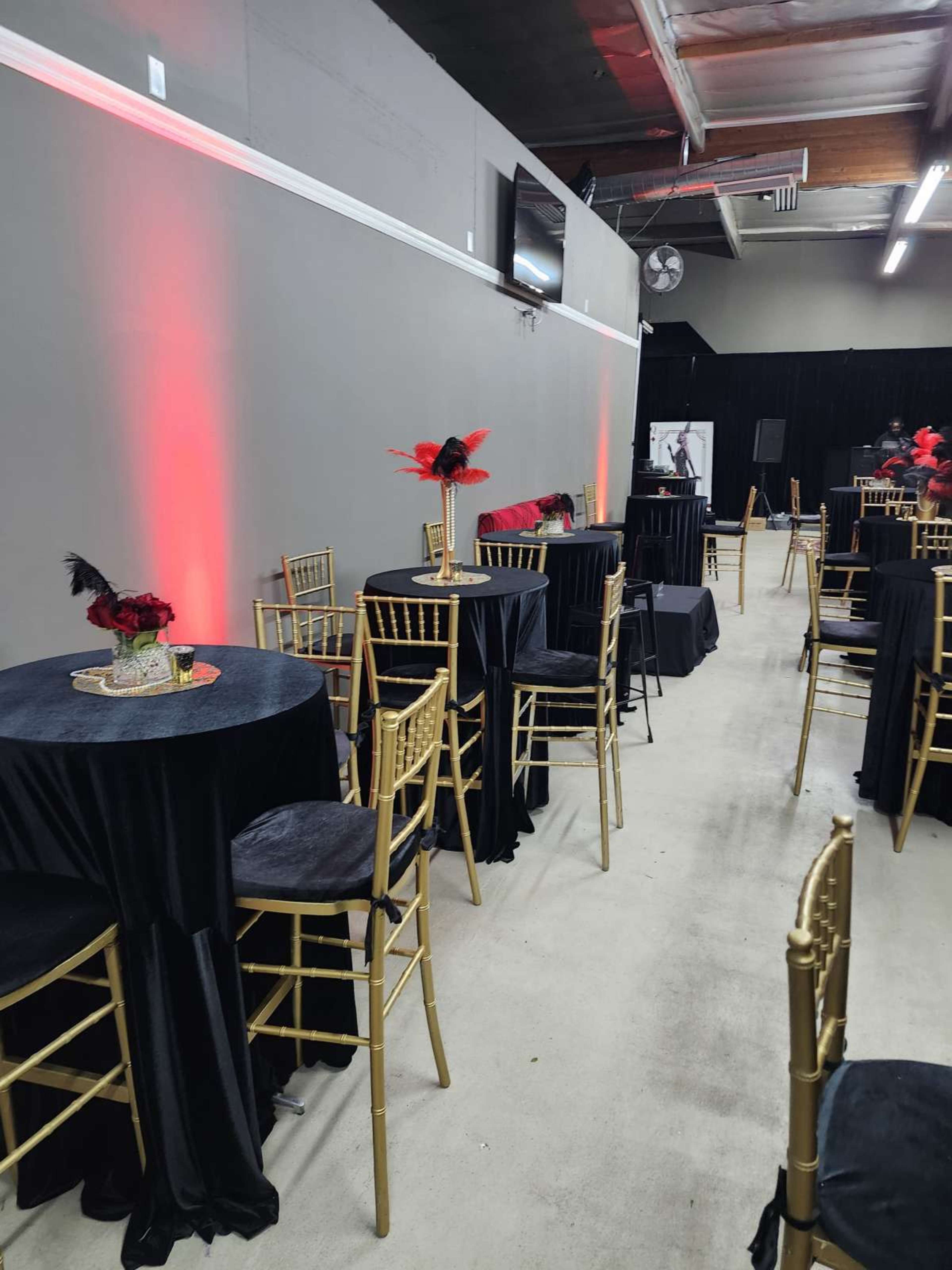 The image shows a banquet space with round tables covered in black cloth, gold chairs, and red lighting accents.