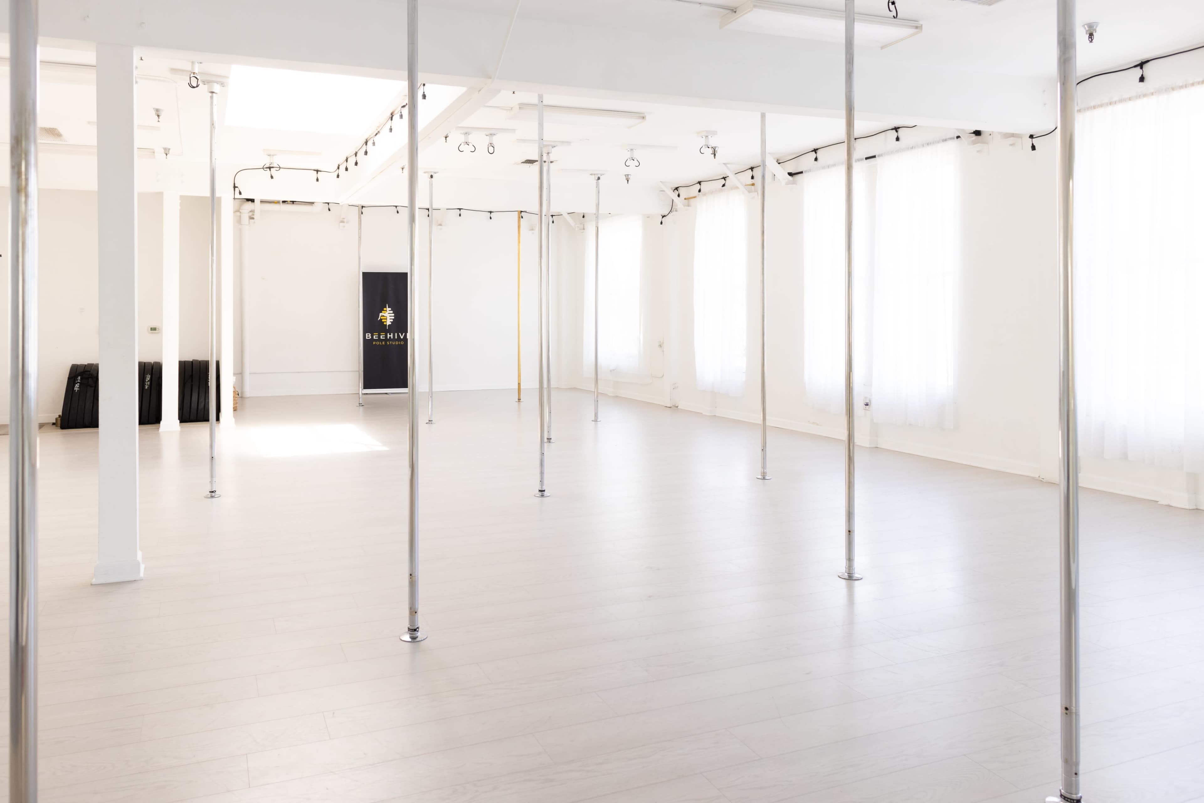 The image shows a bright, clean studio space with several vertical poles and large windows allowing natural light to enter.