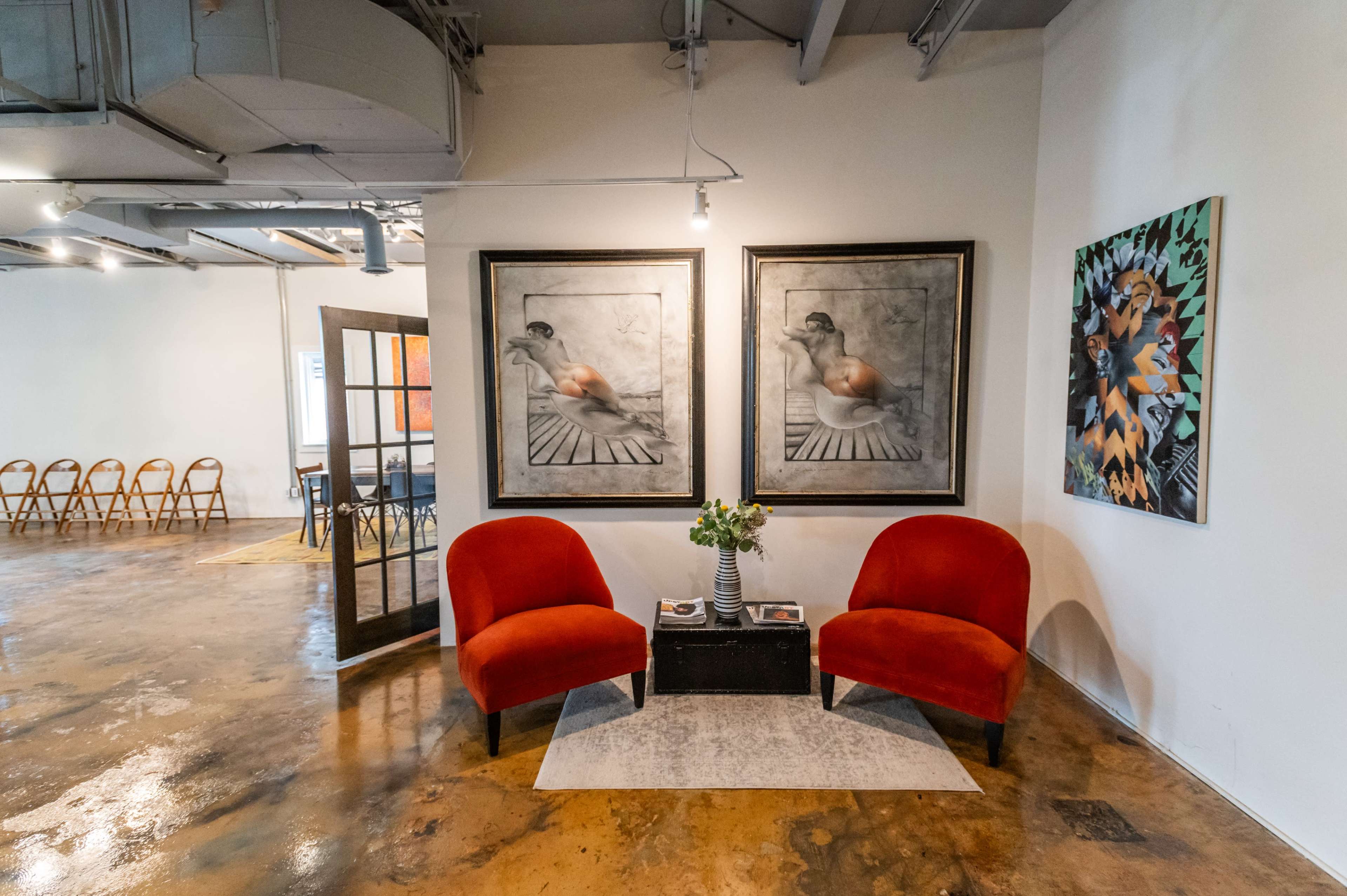A modern interior space featuring two red armchairs, a small table with flowers, and artwork on the walls.