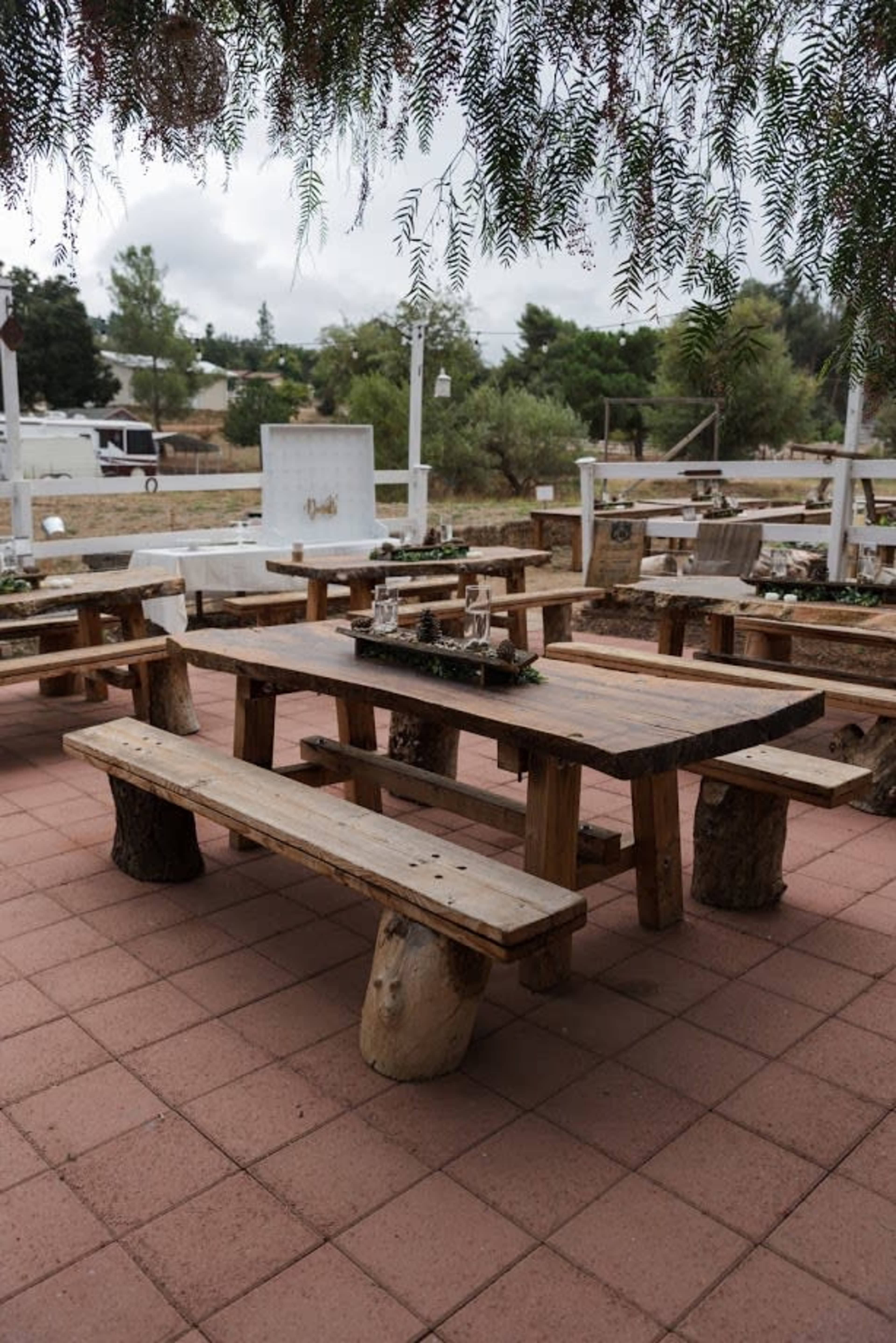 The image shows a rustic outdoor seating area with wooden tables and benches set on a tiled patio.