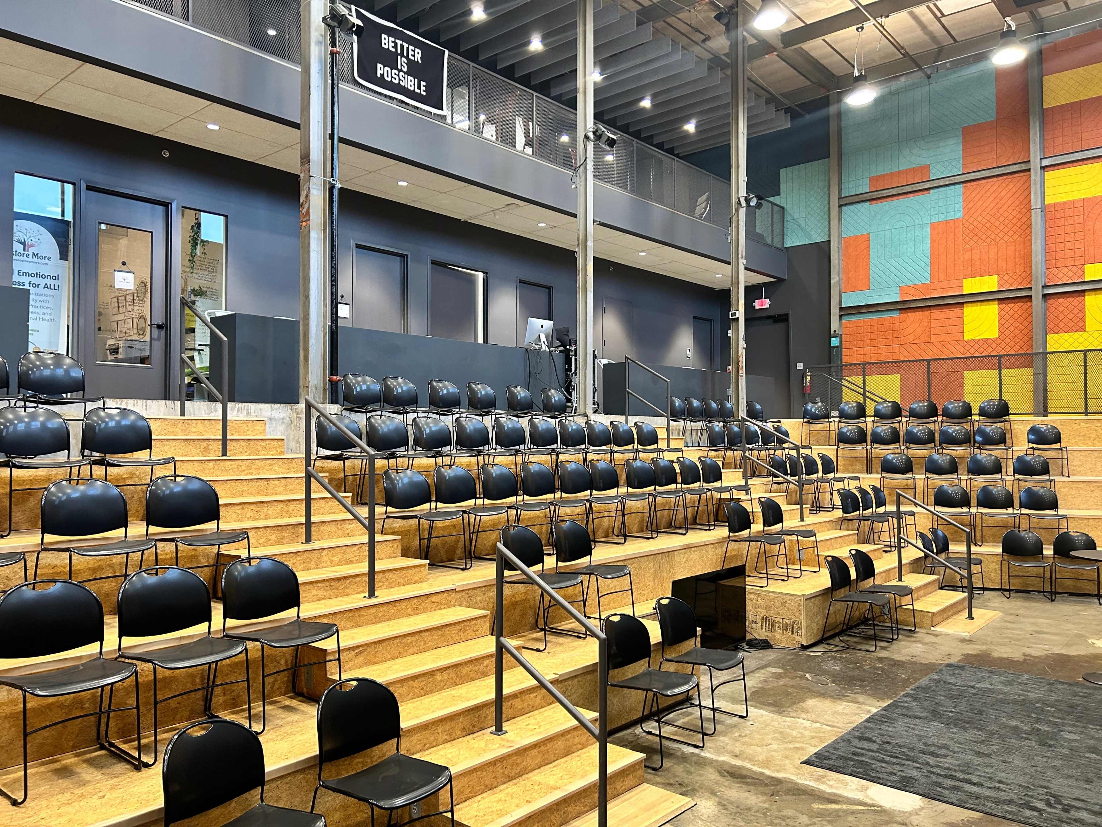 A modern auditorium with tiered wooden seating and black chairs arranged for an event.