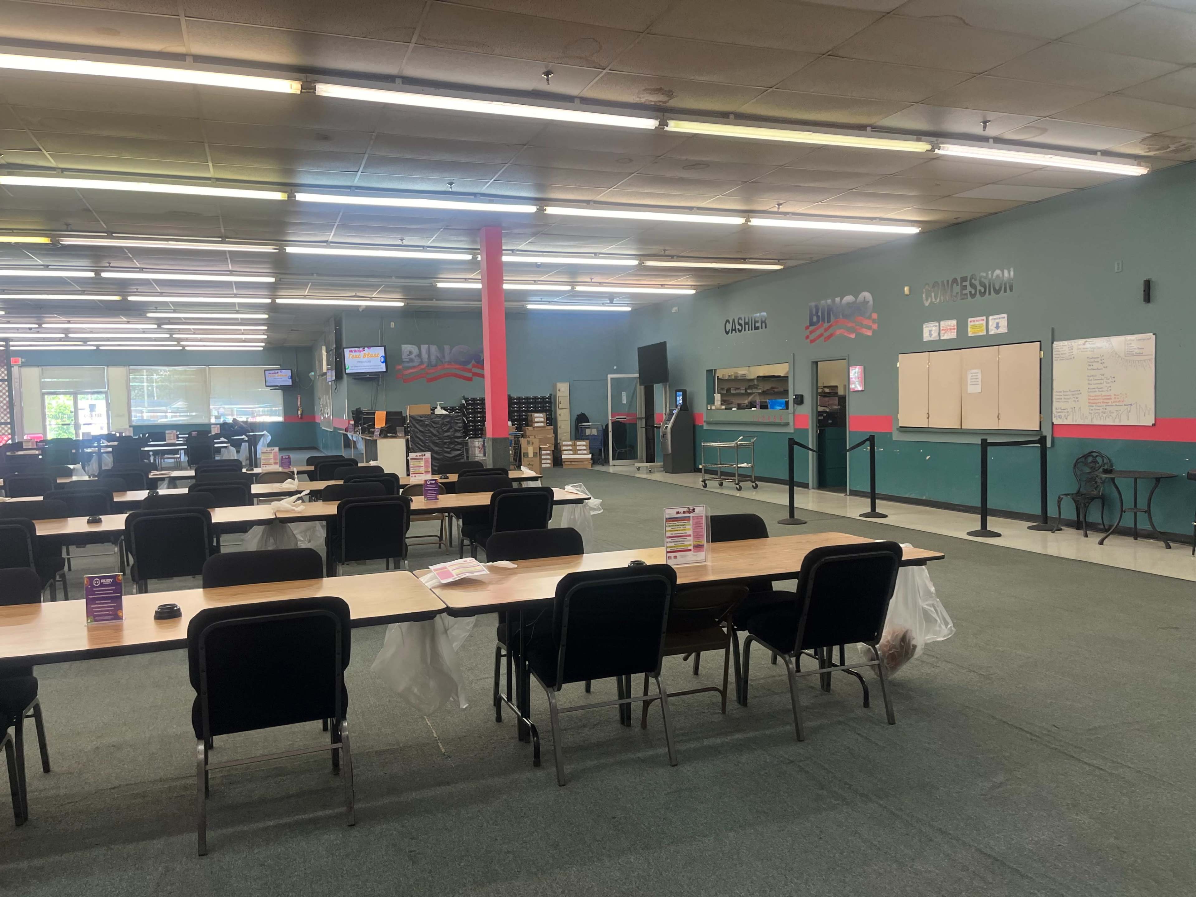 A spacious bingo hall with tables set up in rows, chairs positioned around them, and a cashier area visible in the background.