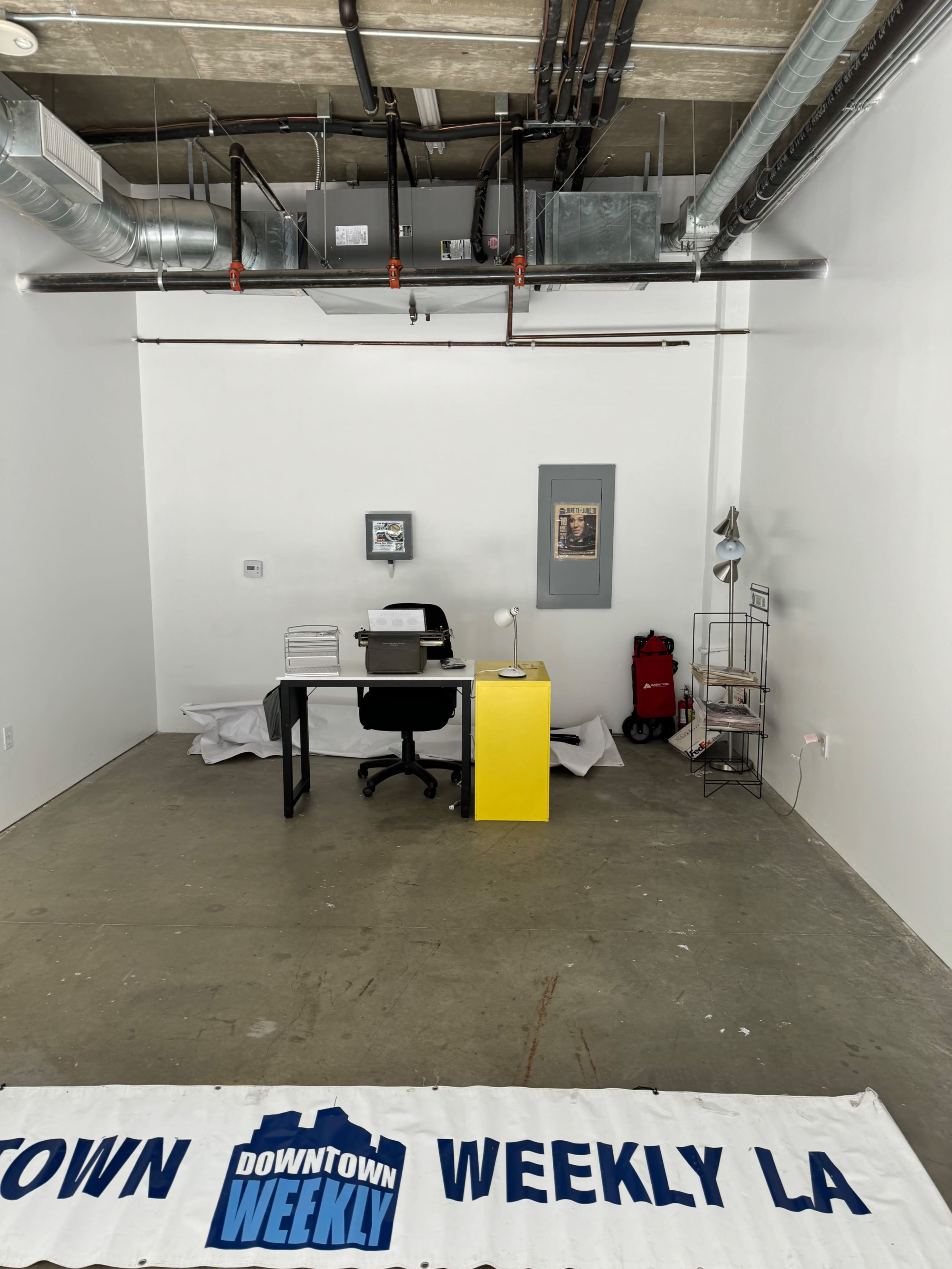 An empty office space features a desk with a chair, a yellow cabinet, and a banner on the floor.
