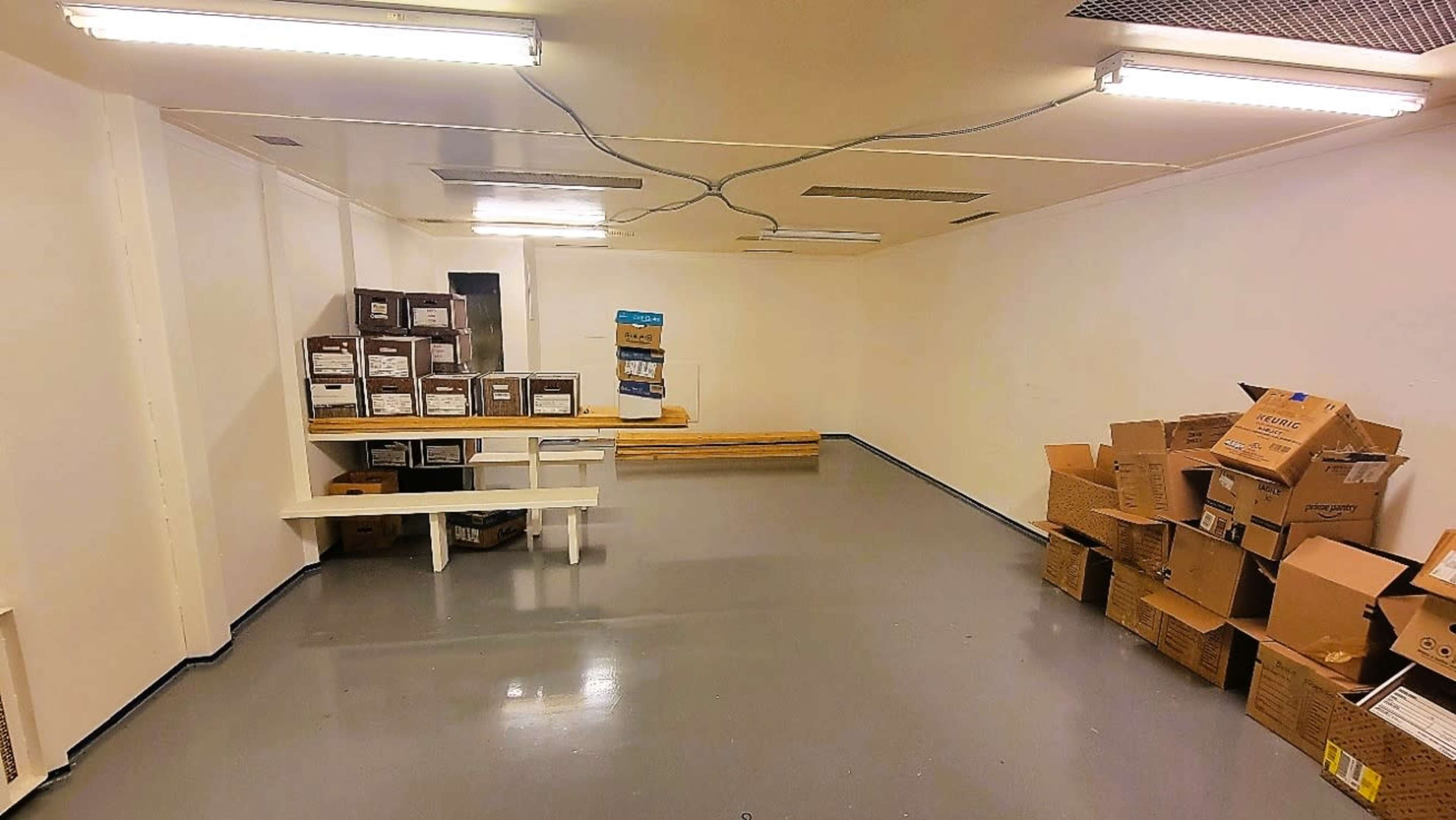 An empty storage room with stacked cardboard boxes and a set of shelves against the wall.