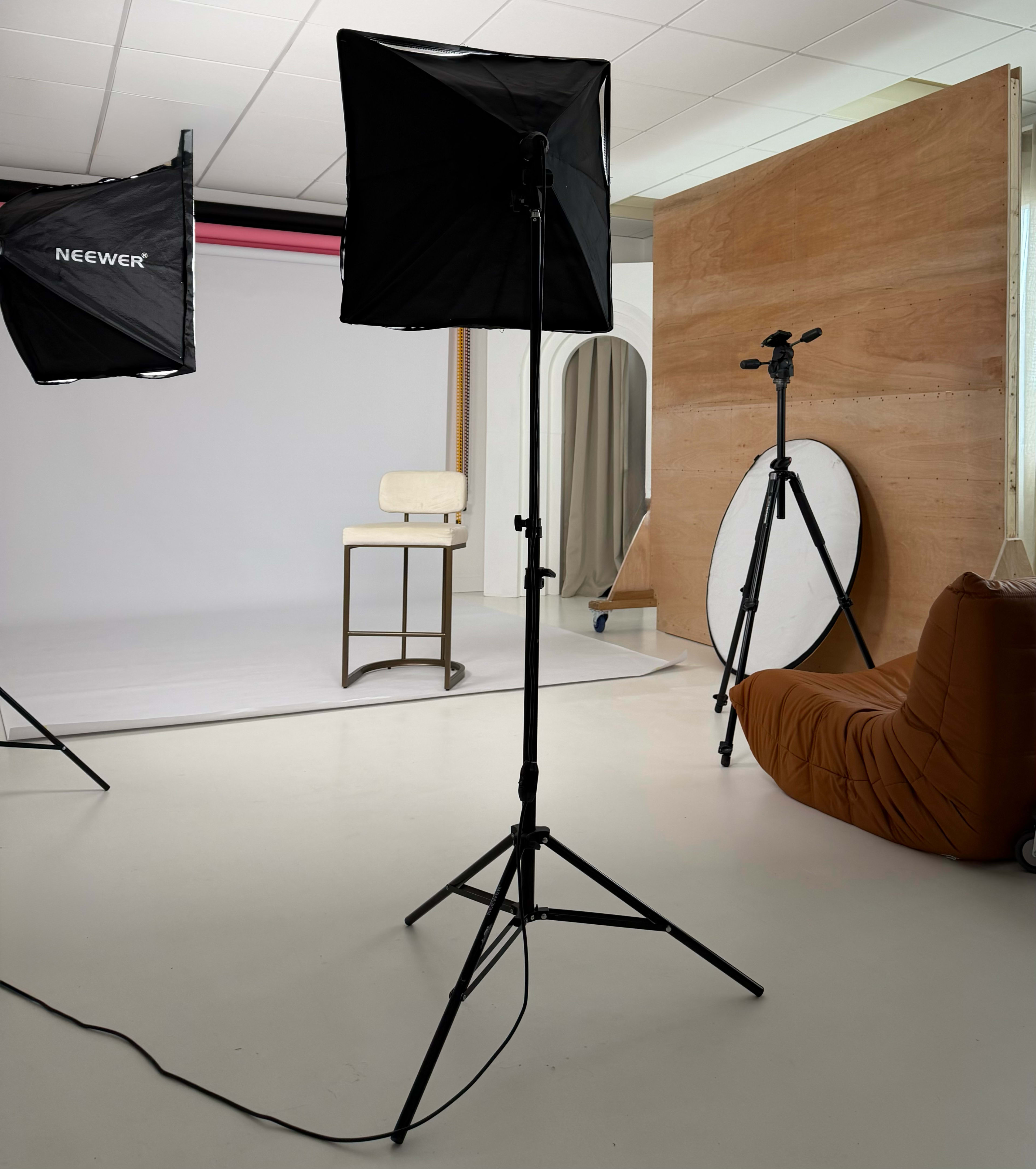 The image shows a photography studio with softboxes, a chair, a backdrop, and a reflector on a stand.