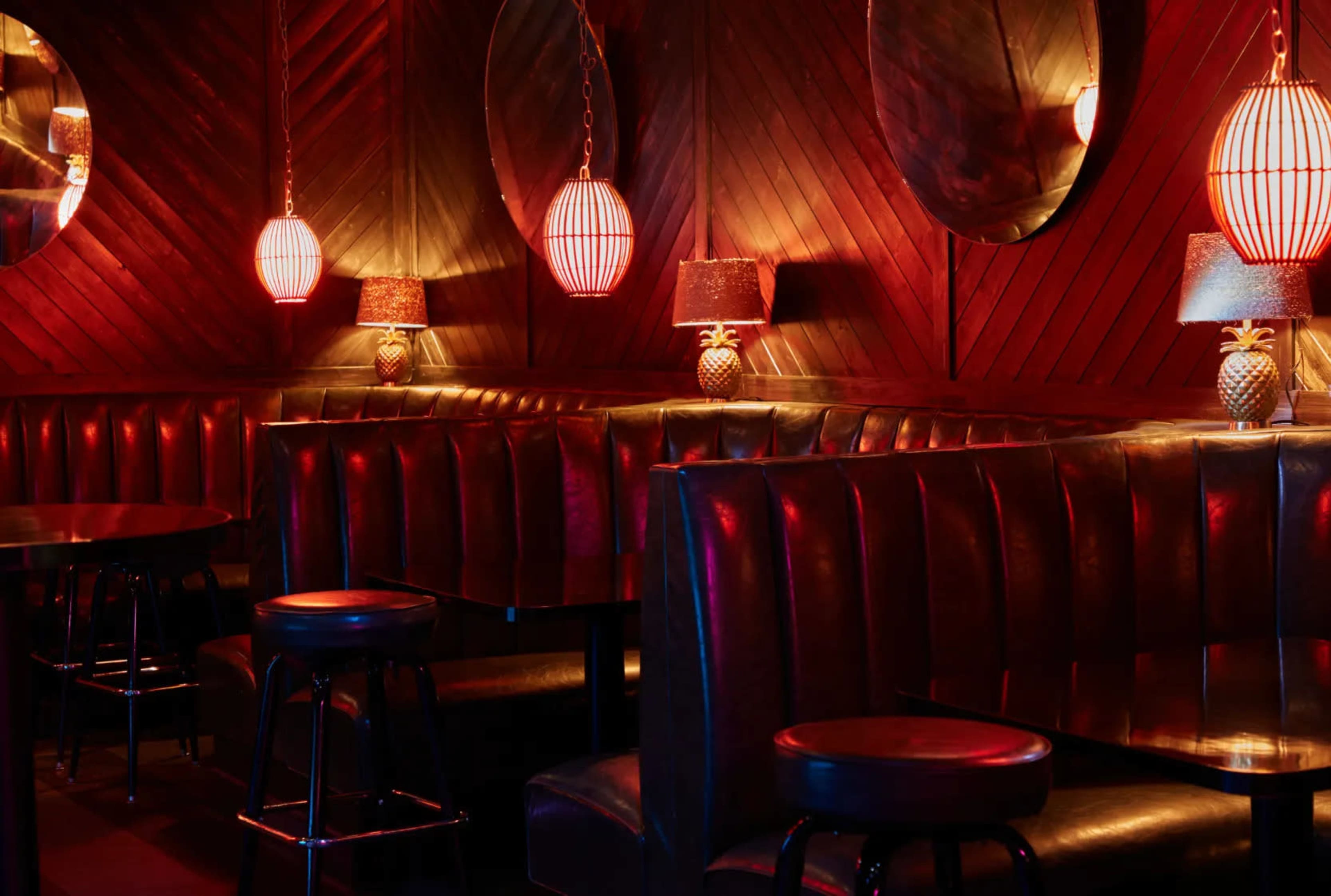The image shows a dimly lit lounge with plush seating, circular mirrors, and red pendant lights.
