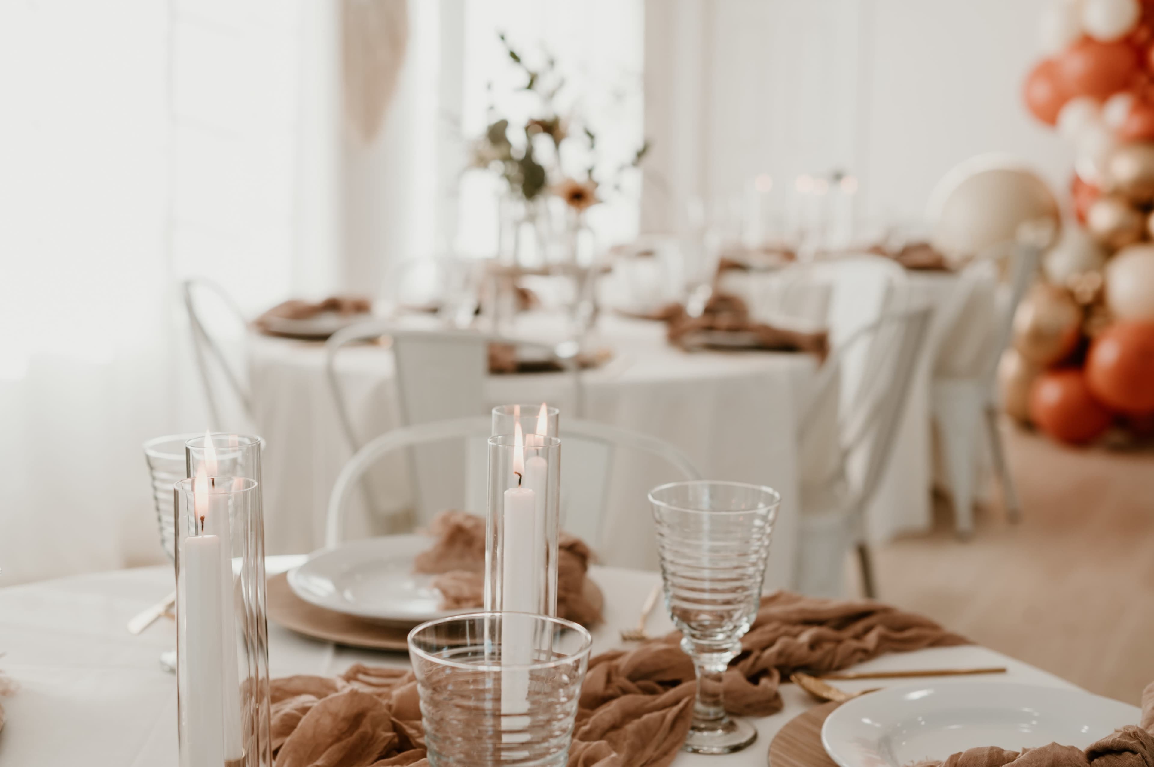 A dining setting features elegantly arranged tables with white tablecloths, clear glassware, and lit candles.