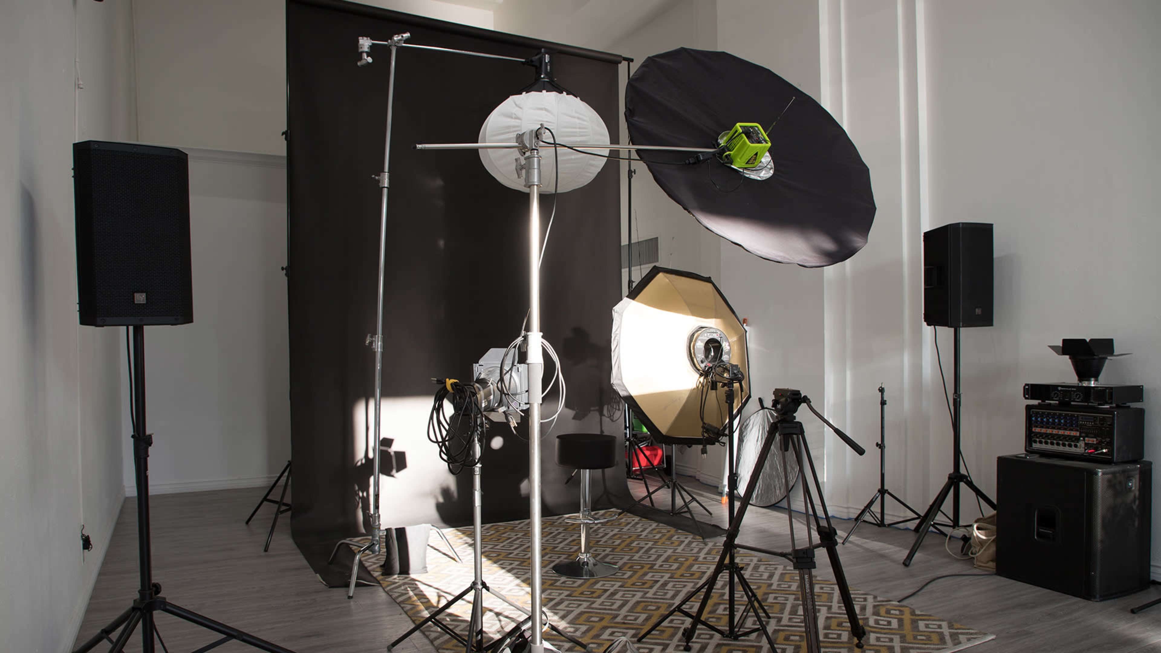A photography studio setup with various lighting equipment, backdrop, and accessories arranged on a patterned rug.