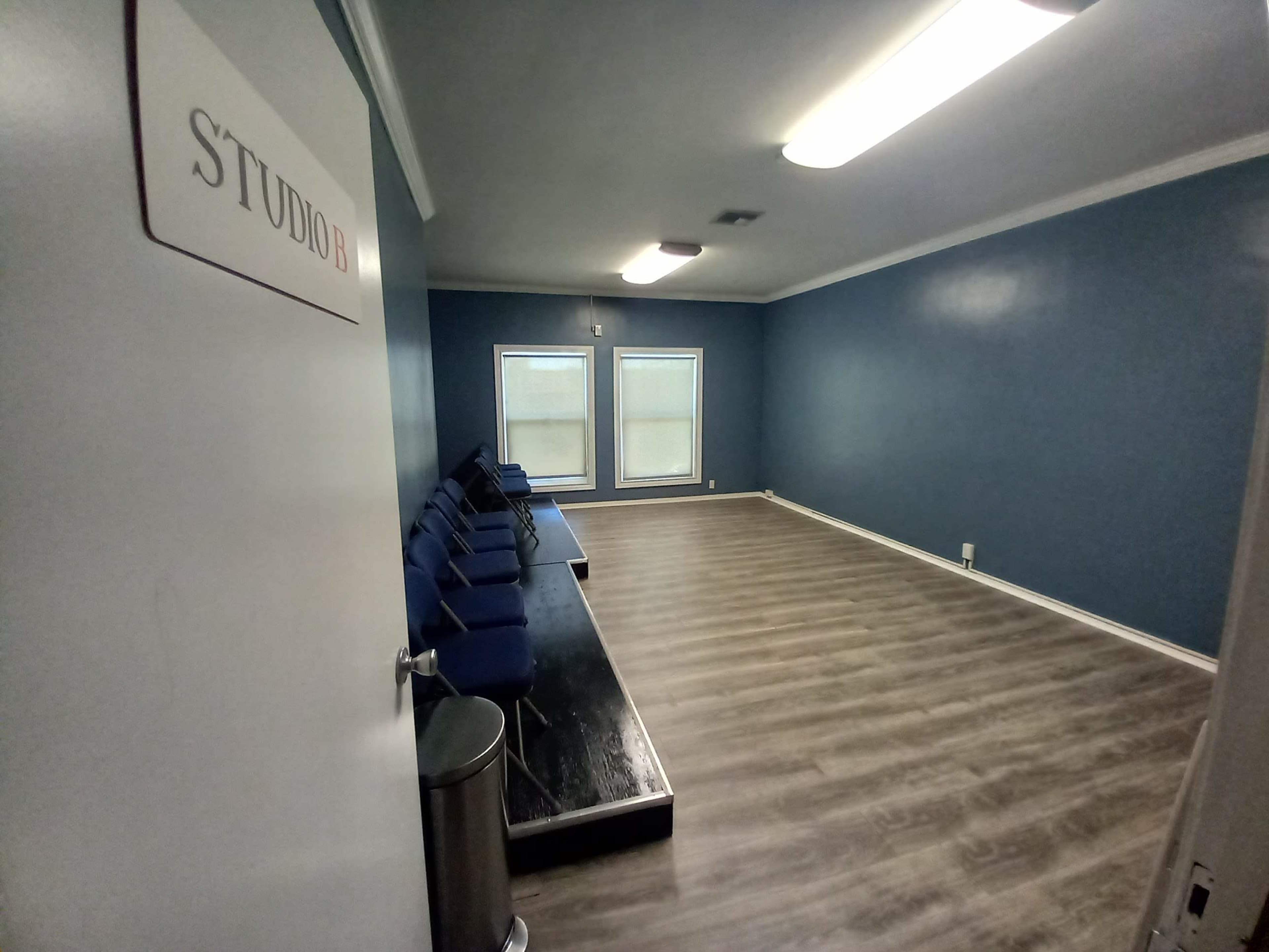 A small room labeled "STUDIO B" with blue walls, a row of blue chairs against the far wall, and two windows allowing natural light.