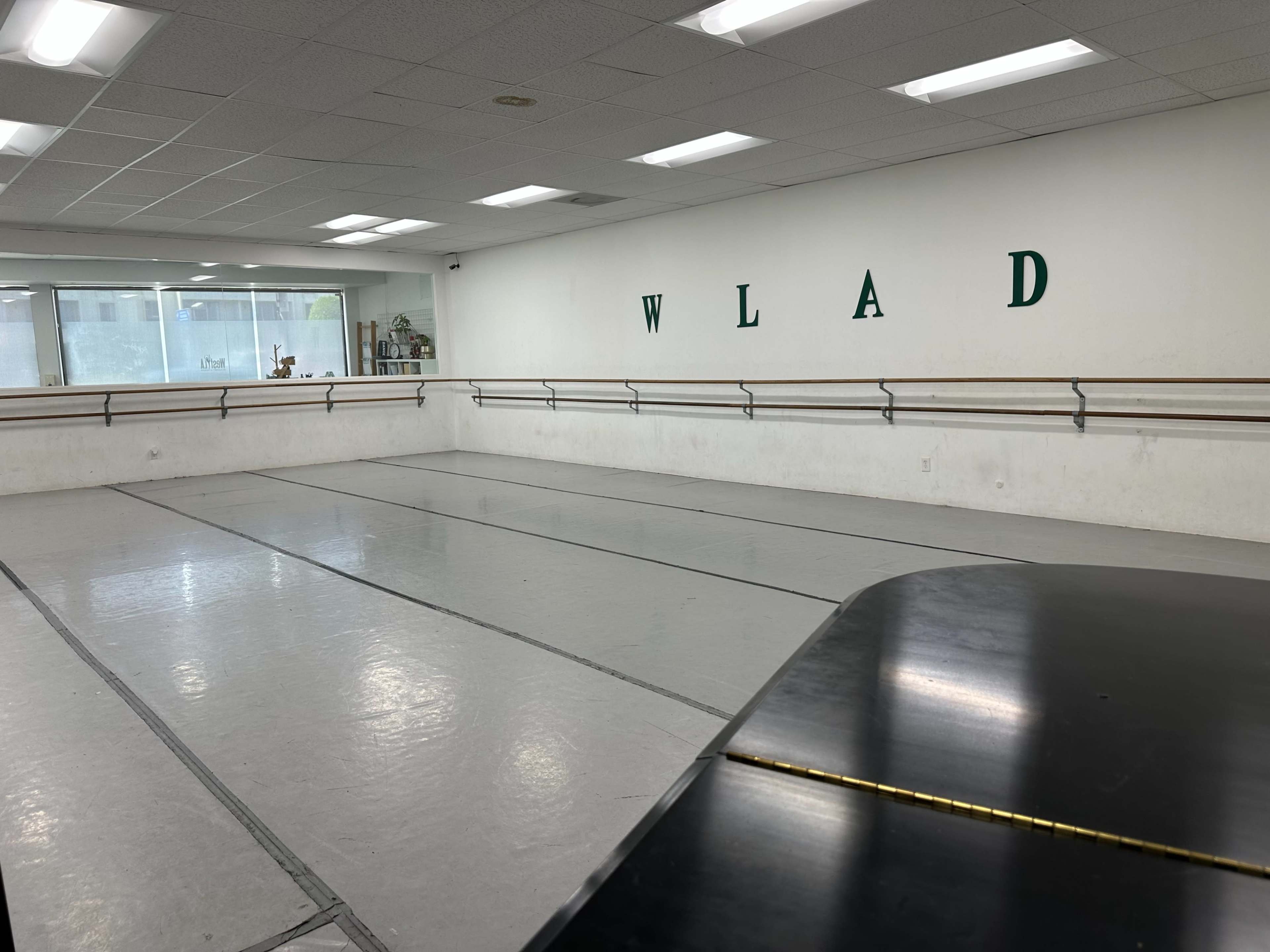 The image shows a spacious dance studio with barre rails along the walls and a piano in the foreground.