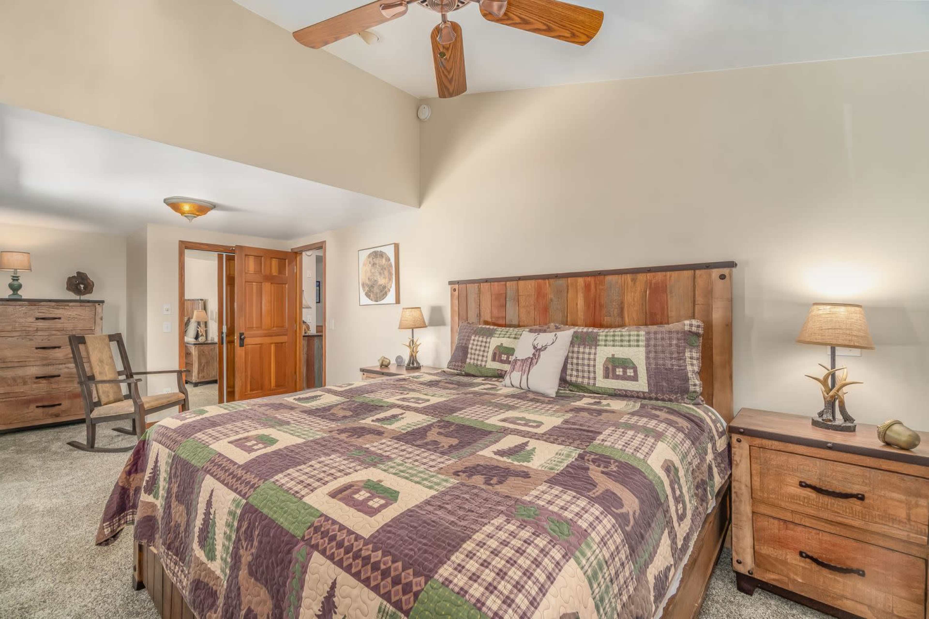 A spacious bedroom features a wooden bed with a patterned quilt, matching nightstands, and a dresser, all set against a neutral wall and carpet.
