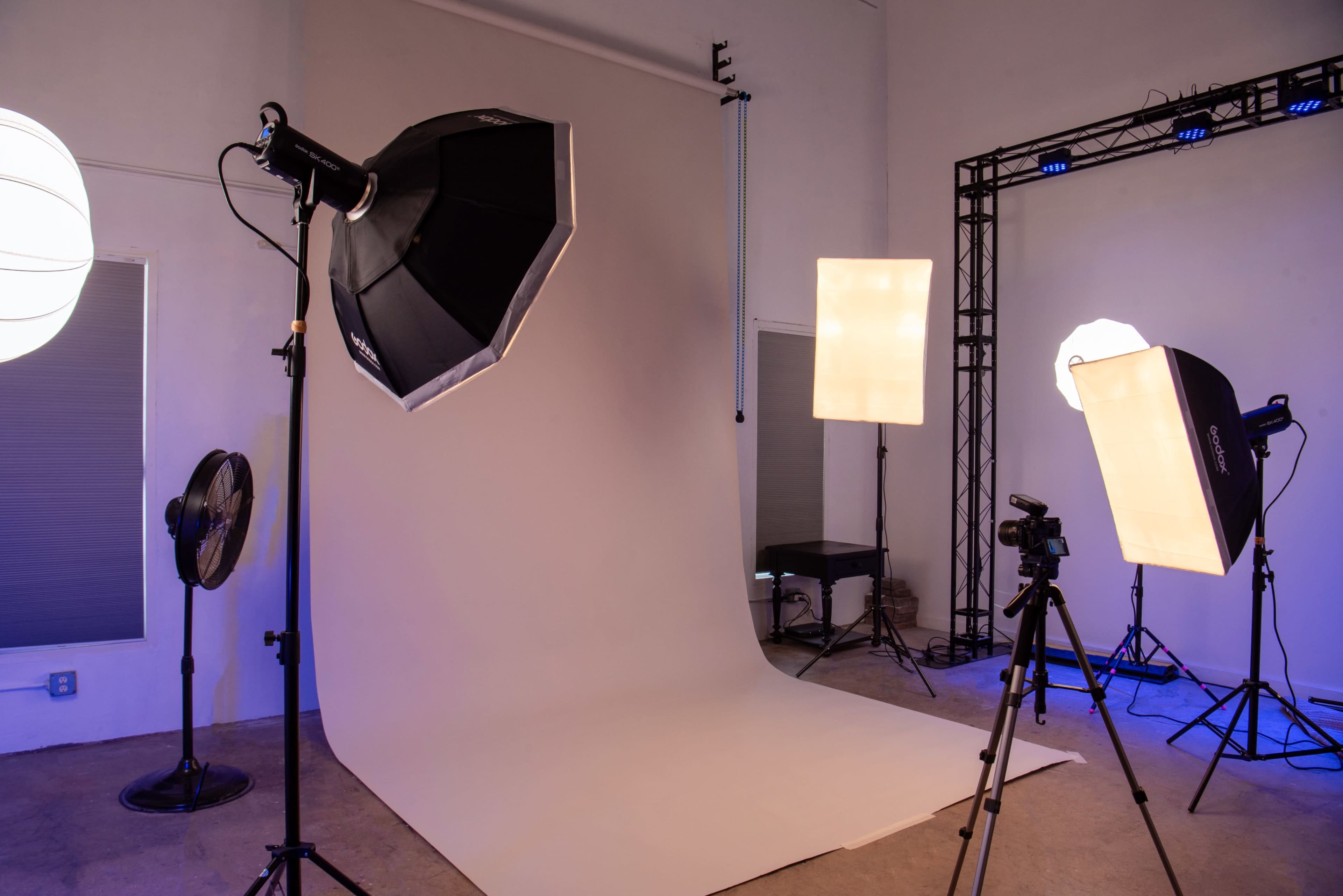 The image shows a photography studio equipped with various lighting setups, a backdrop, and a camera tripod.