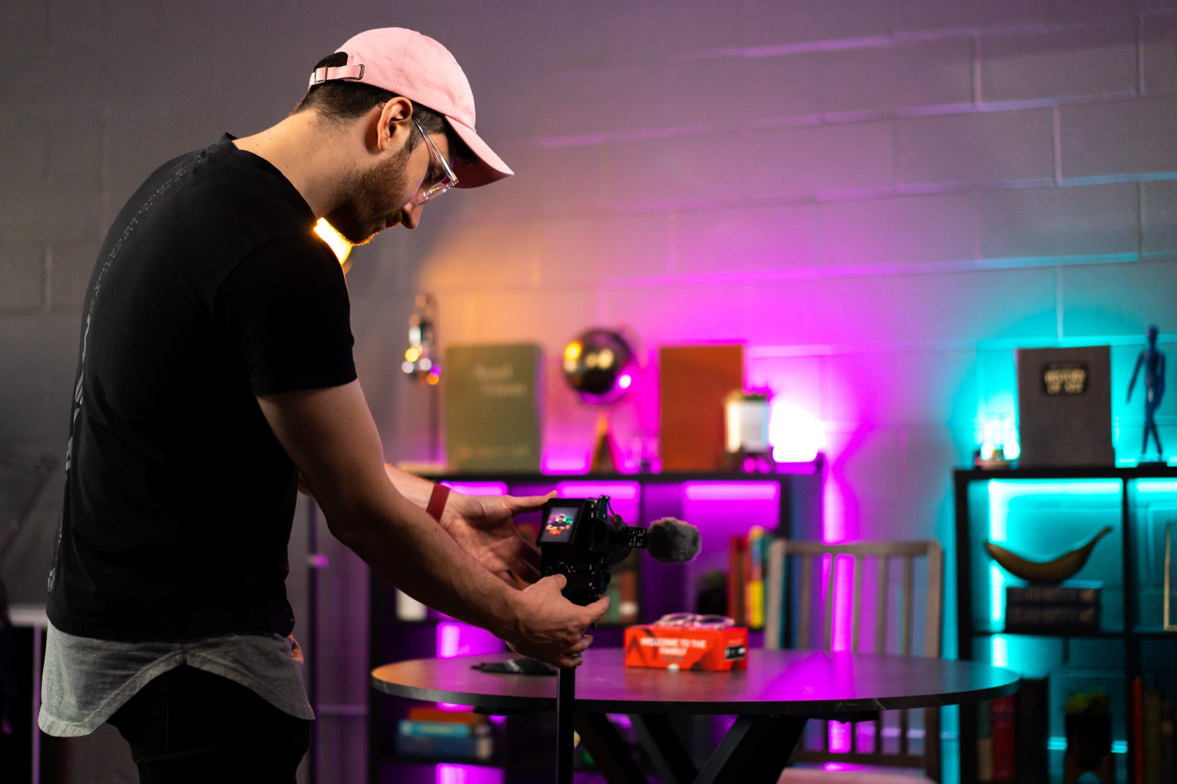 A man adjusts a camera on a tripod in a brightly colored, modern workspace.