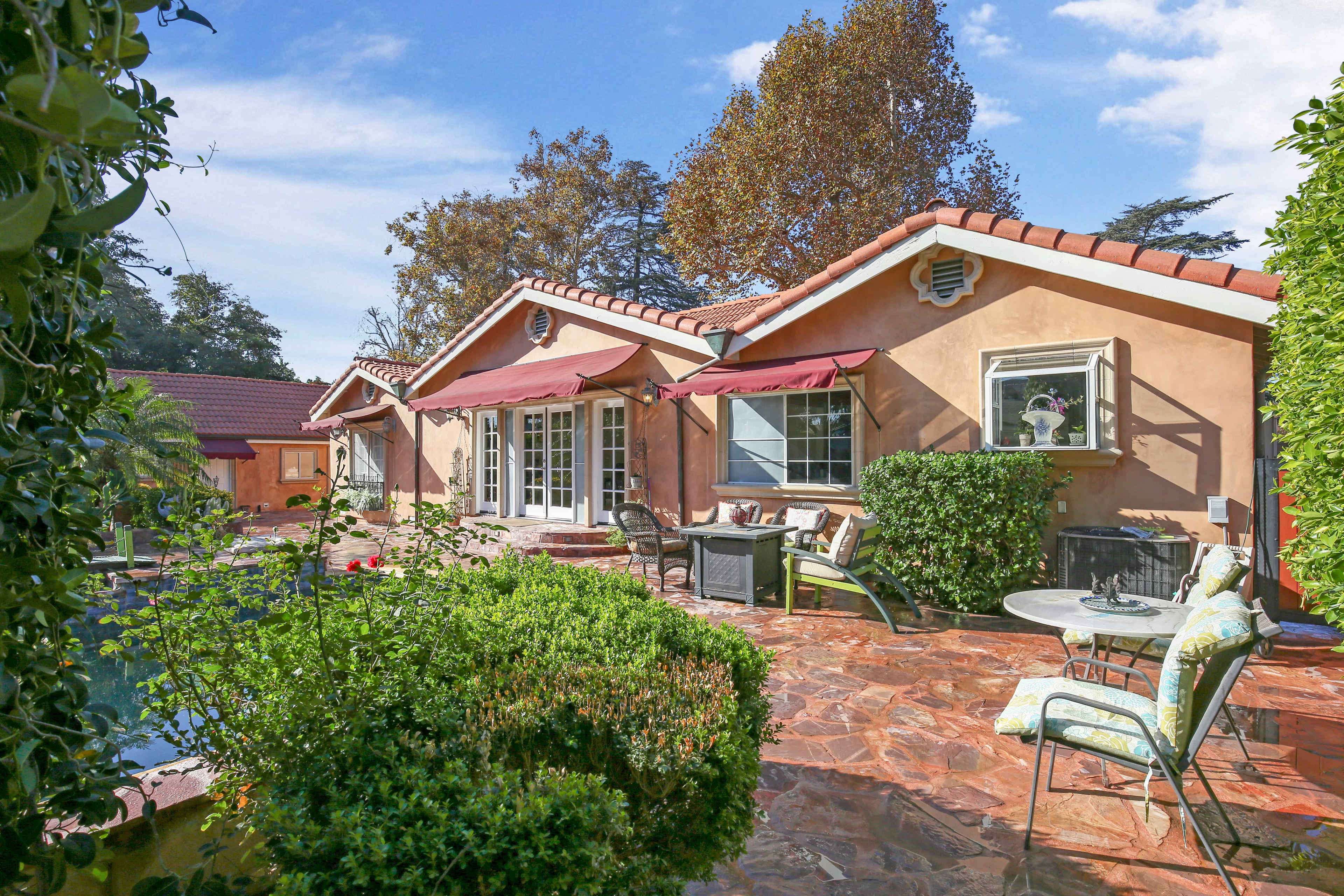 A single-story home with a terracotta roof features a patio area surrounded by greenery and a swimming pool.