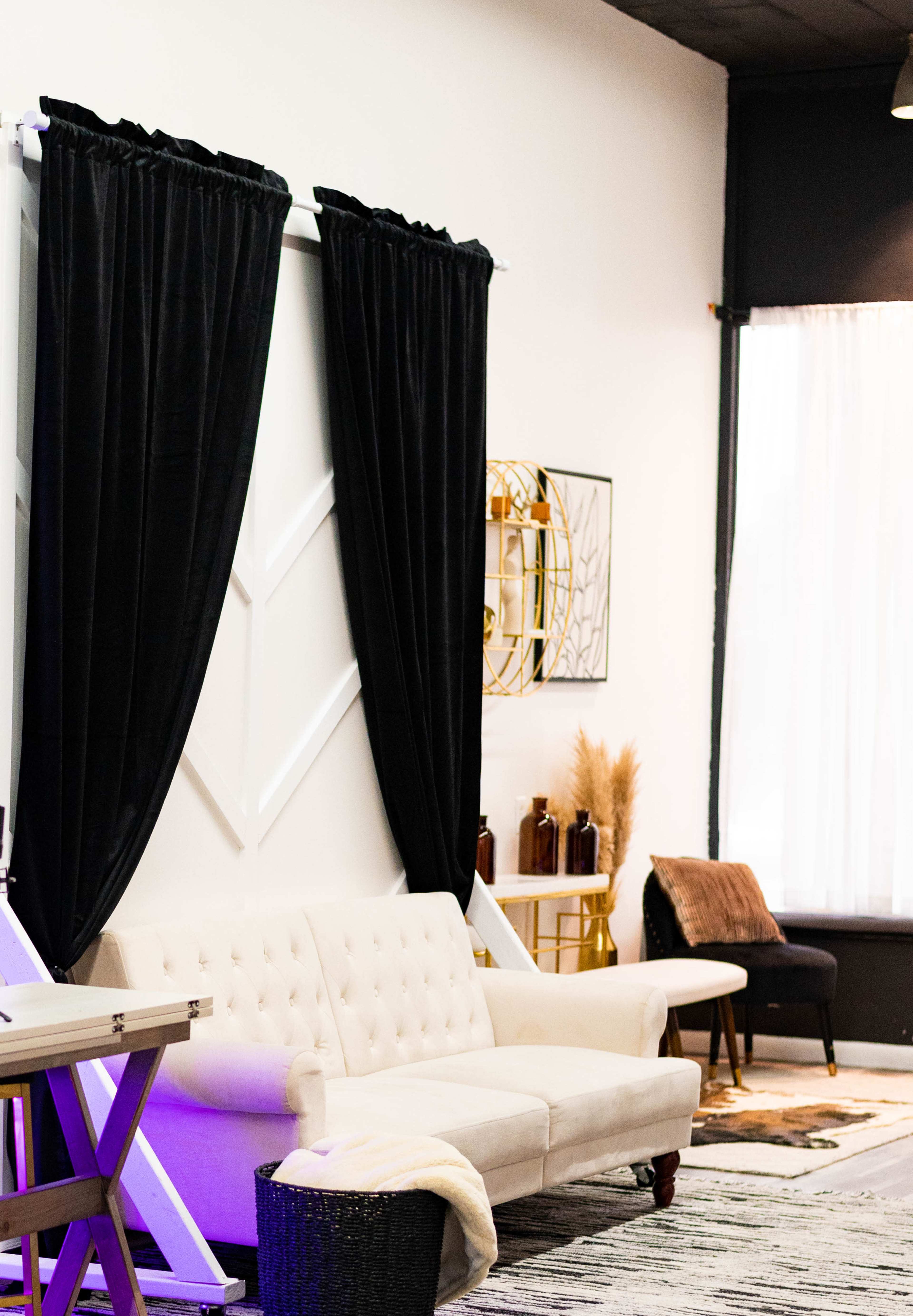 A modern interior space with a light-colored couch, black curtains, wall decor, and a decorative chair near a window.