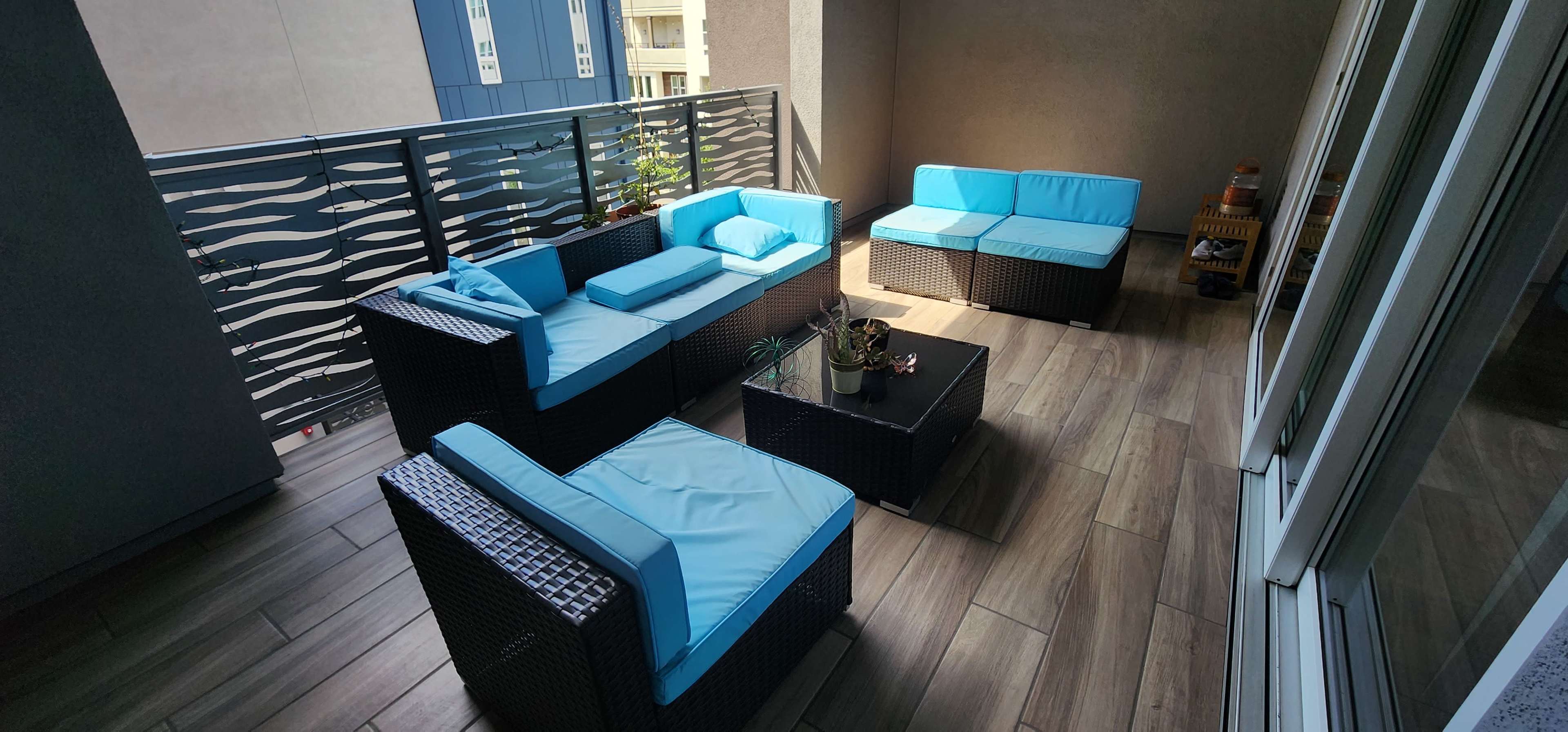 A modern balcony features wicker furniture with light blue cushions and a small potted plant on a table.