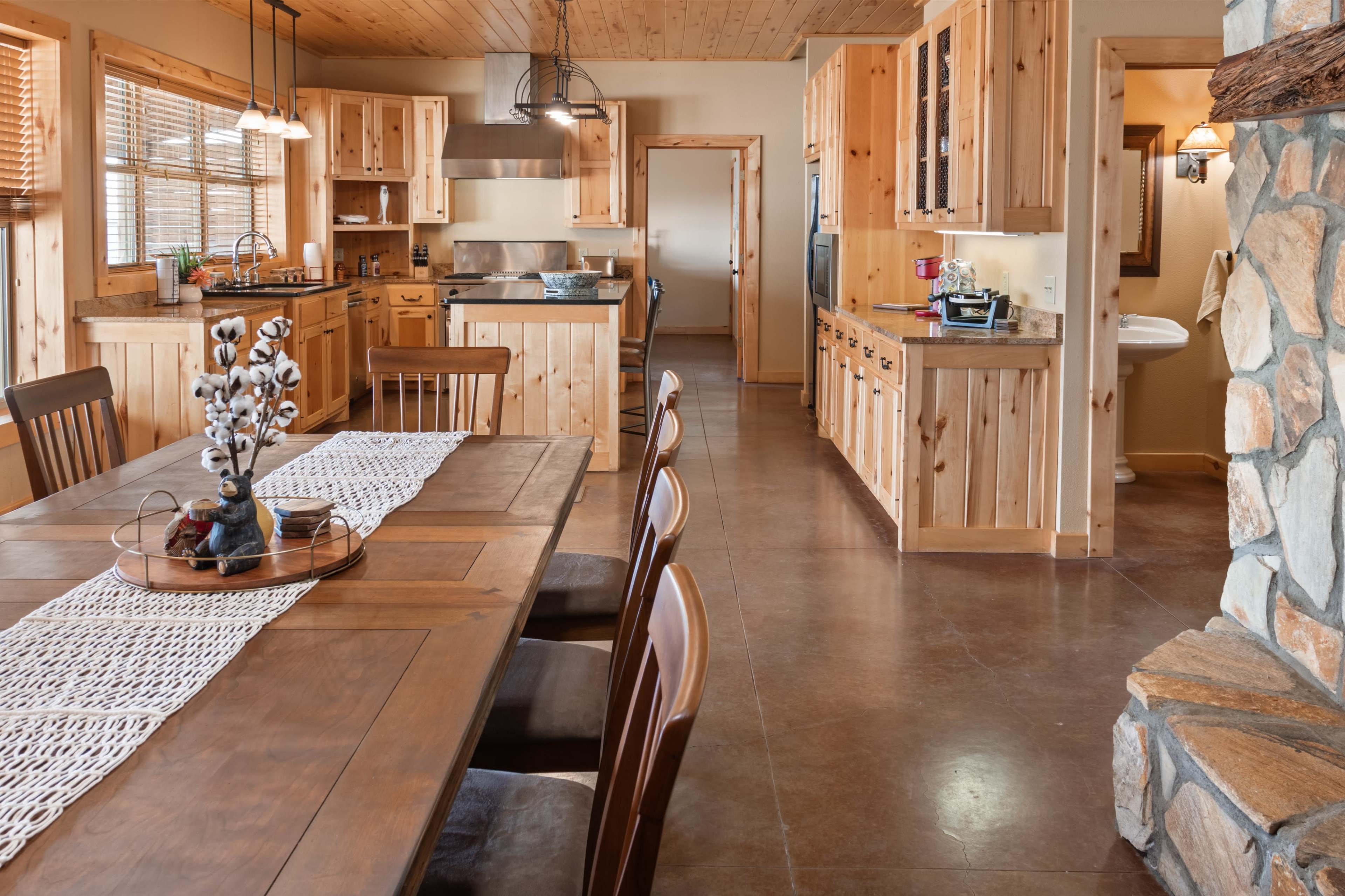 A spacious kitchen and dining area feature wooden cabinets, a large wooden table, and a stone fireplace.