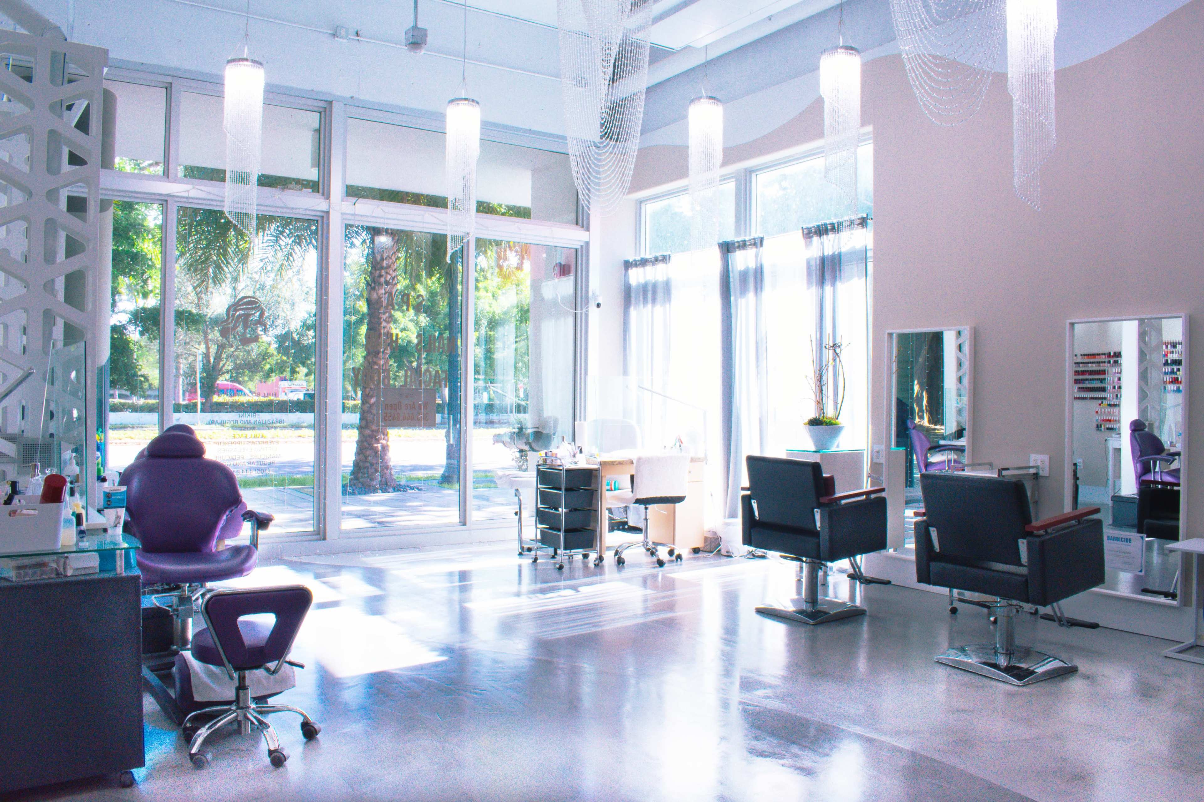 A bright salon interior with two salon chairs, a nail station, and large windows that provide natural light.
