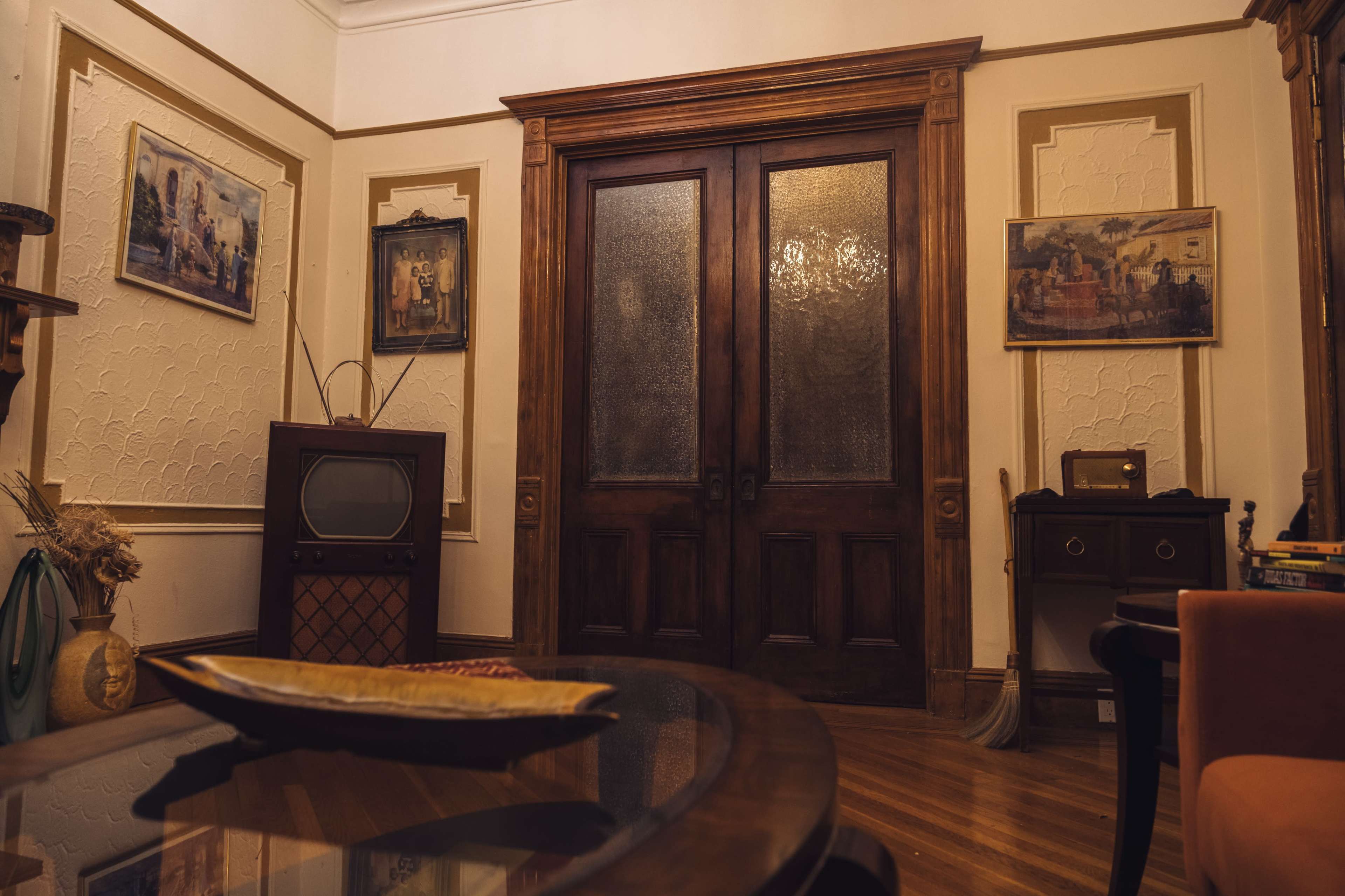 The image shows an interior space featuring a large set of wooden double doors, framed by ornate wall decorations and accompanied by vintage artwork on the walls.