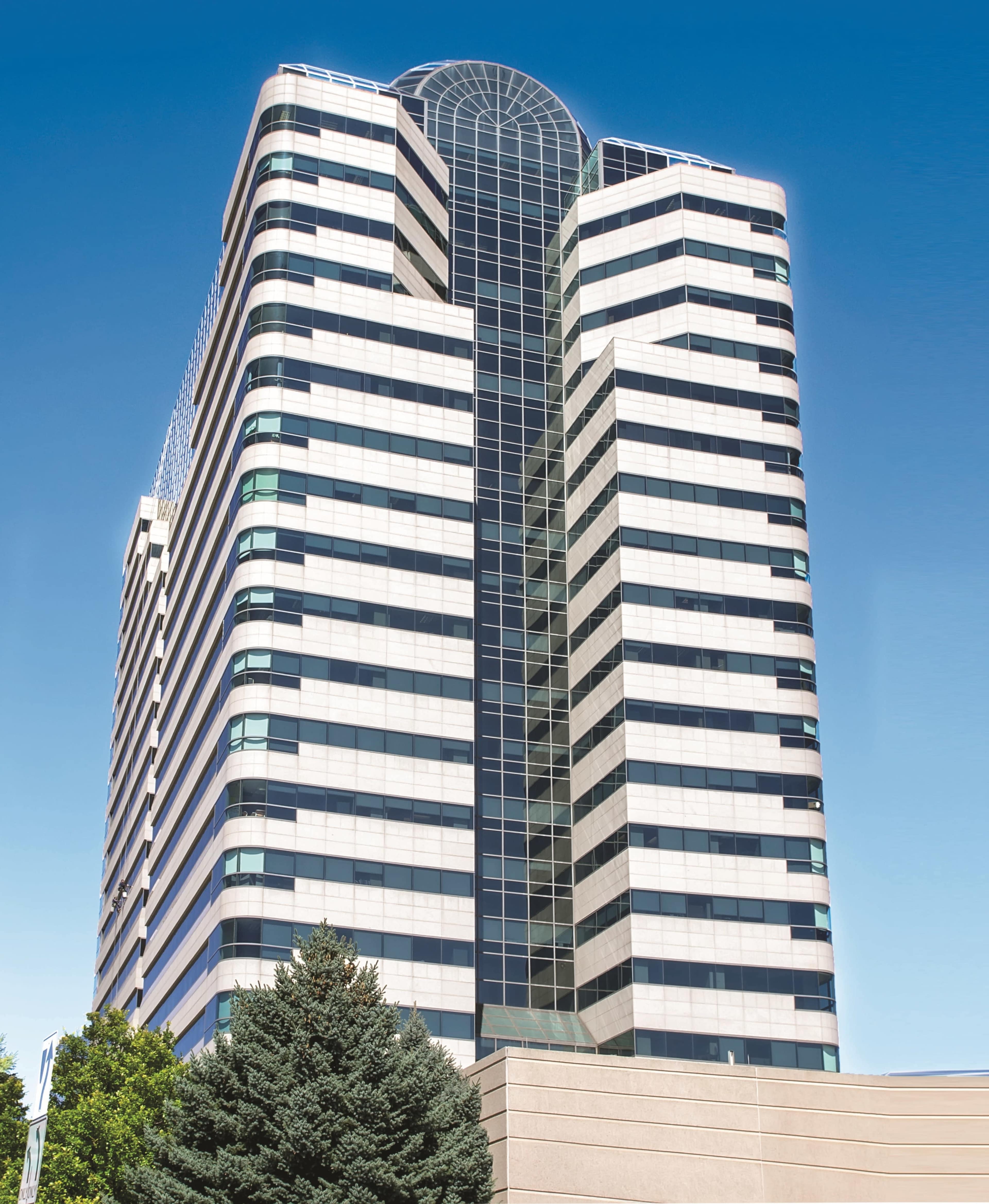 A tall, modern building with a glass and steel facade rises against a clear blue sky.